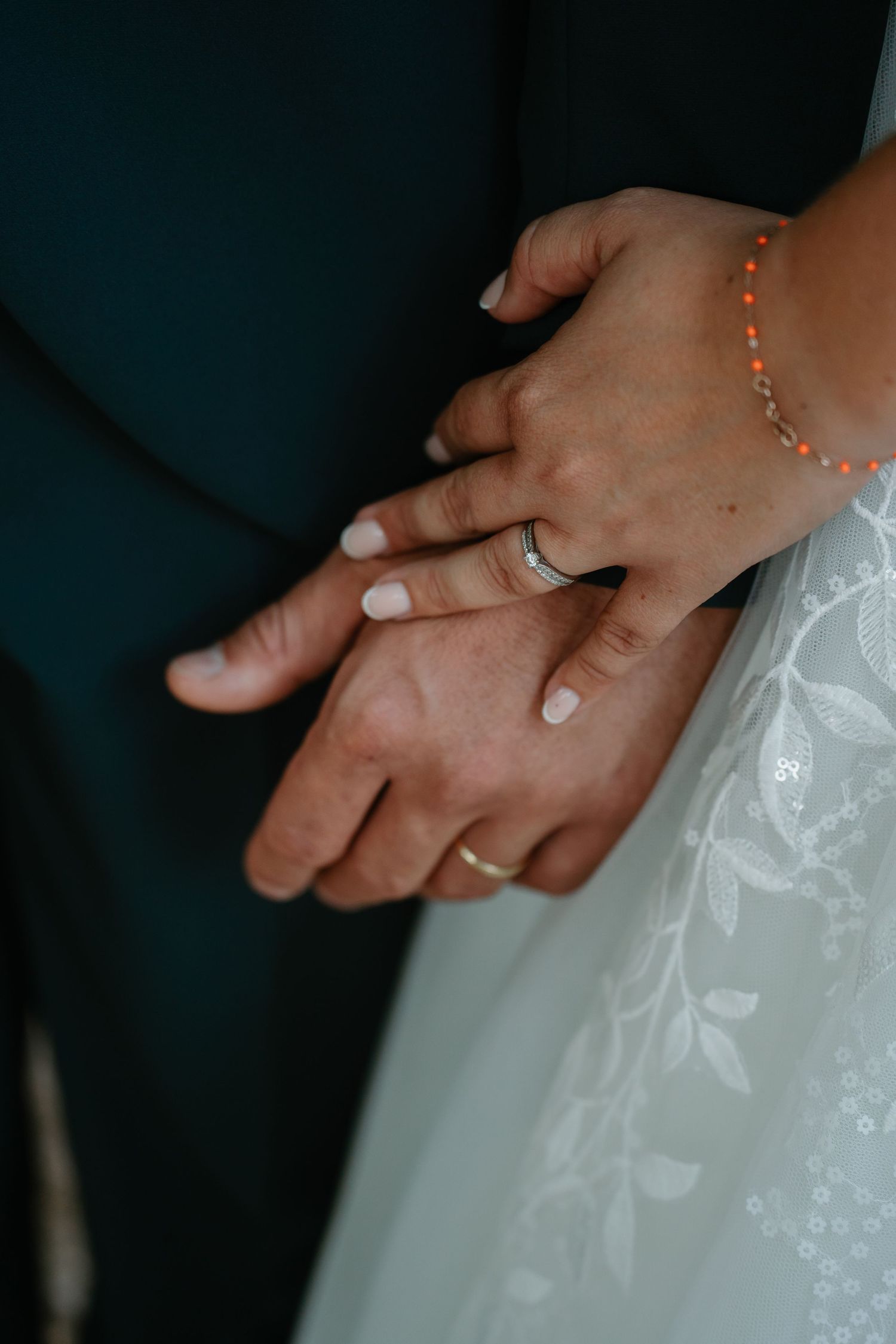 Close-up of hands wearing wedding rings against white lace dress fabric in romantic pose.
