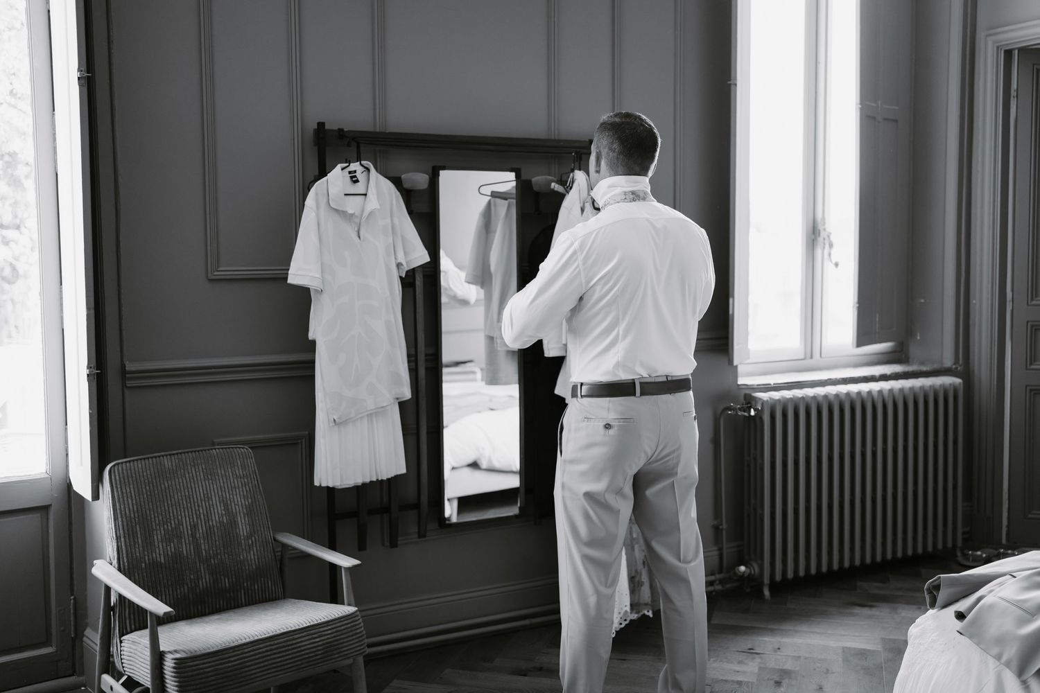 A black and white photograph shows a clinical setting with white coats hanging on a wall and medical equipment visible.
