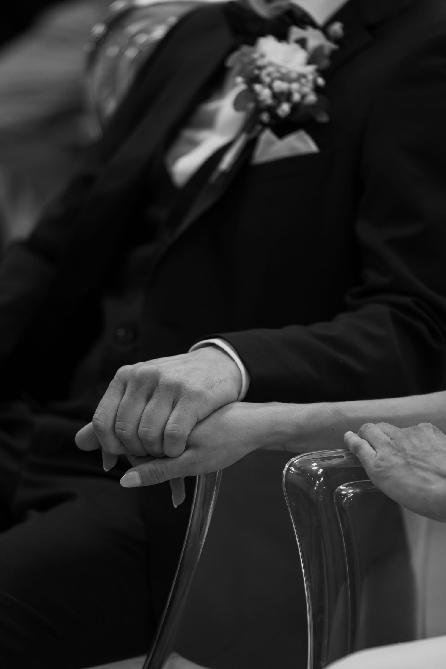 Black and white wedding photo of bride and groom holding hands, groom wearing boutonniere suit.