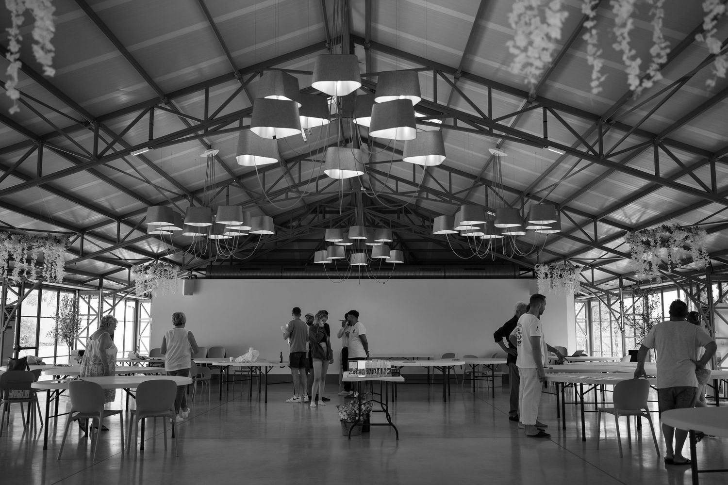 Large industrial warehouse interior with exposed ceiling beams and rows of pendant lights illuminating empty workspaces.