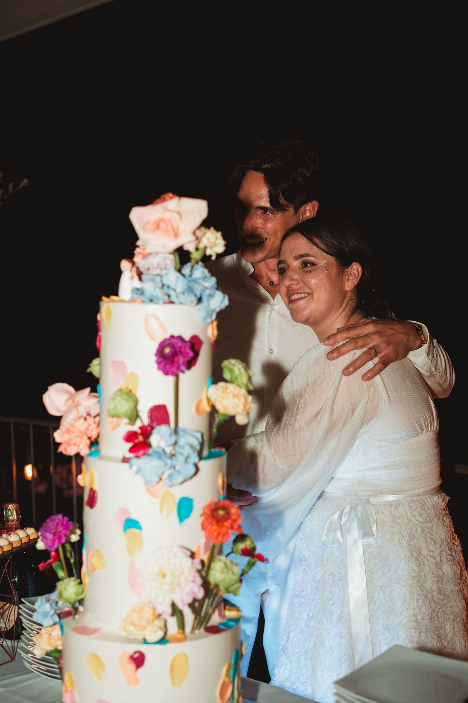 A wedding couple cuts into their colorful floral wedding cake decorated with bright blooms and watercolor details.