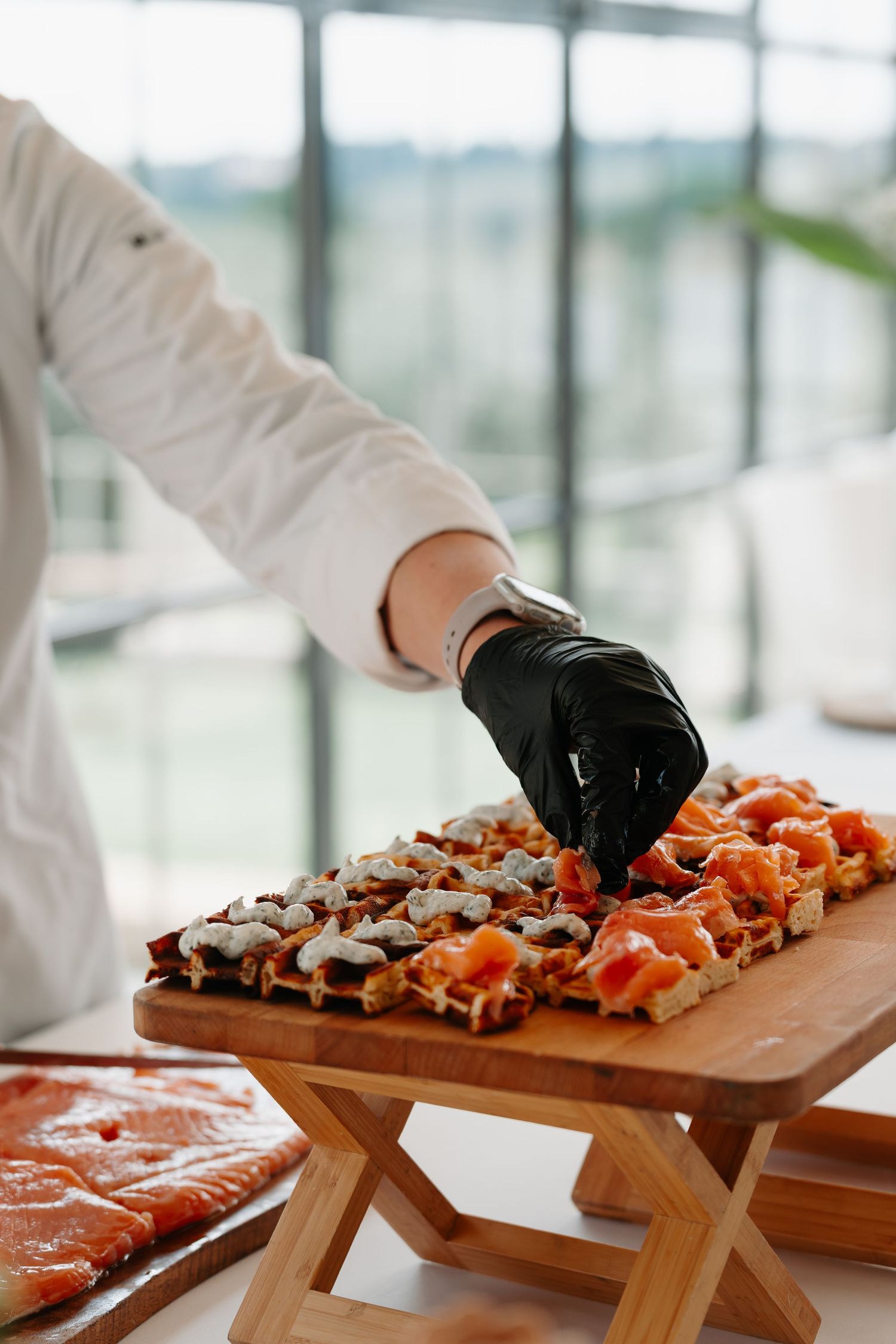 Chef wearing black gloves arranges fresh seafood and meat on wooden serving boards for catering display.