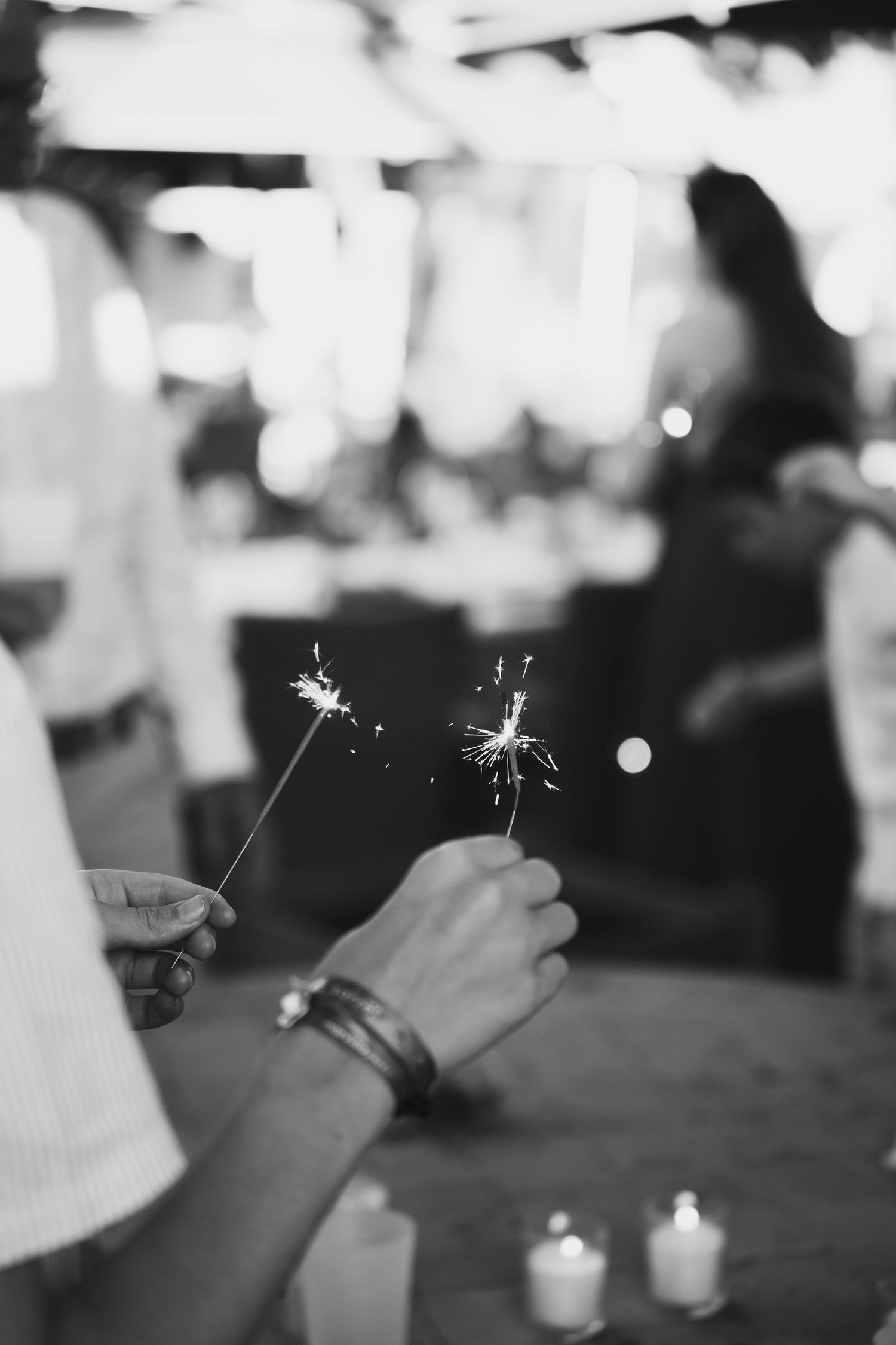 A row of hands holding lit sparklers creates a magical ambiance at a nighttime celebration.