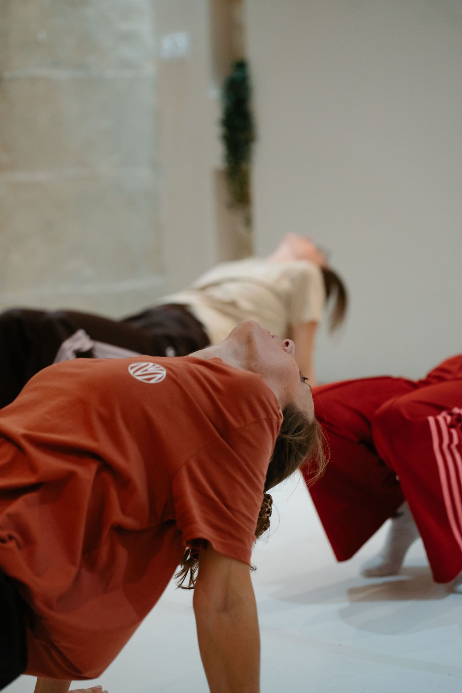 Dancers in red clothing lean forward in synchronized motion during a contemporary dance performance.