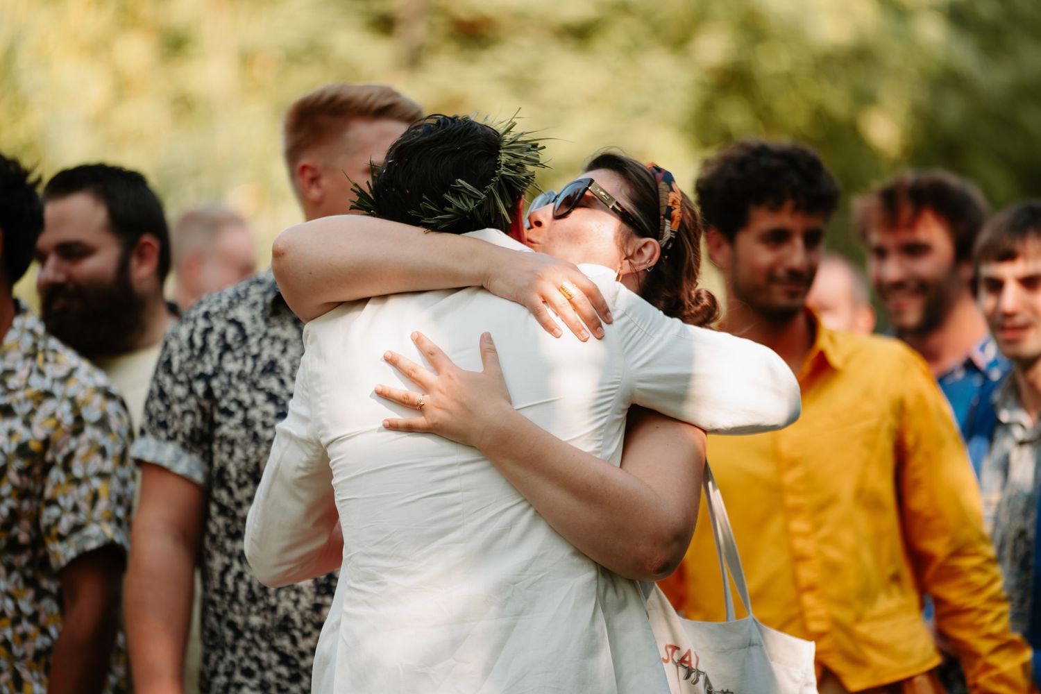 Two people share an emotional embrace at an outdoor gathering while others look on in the background.
