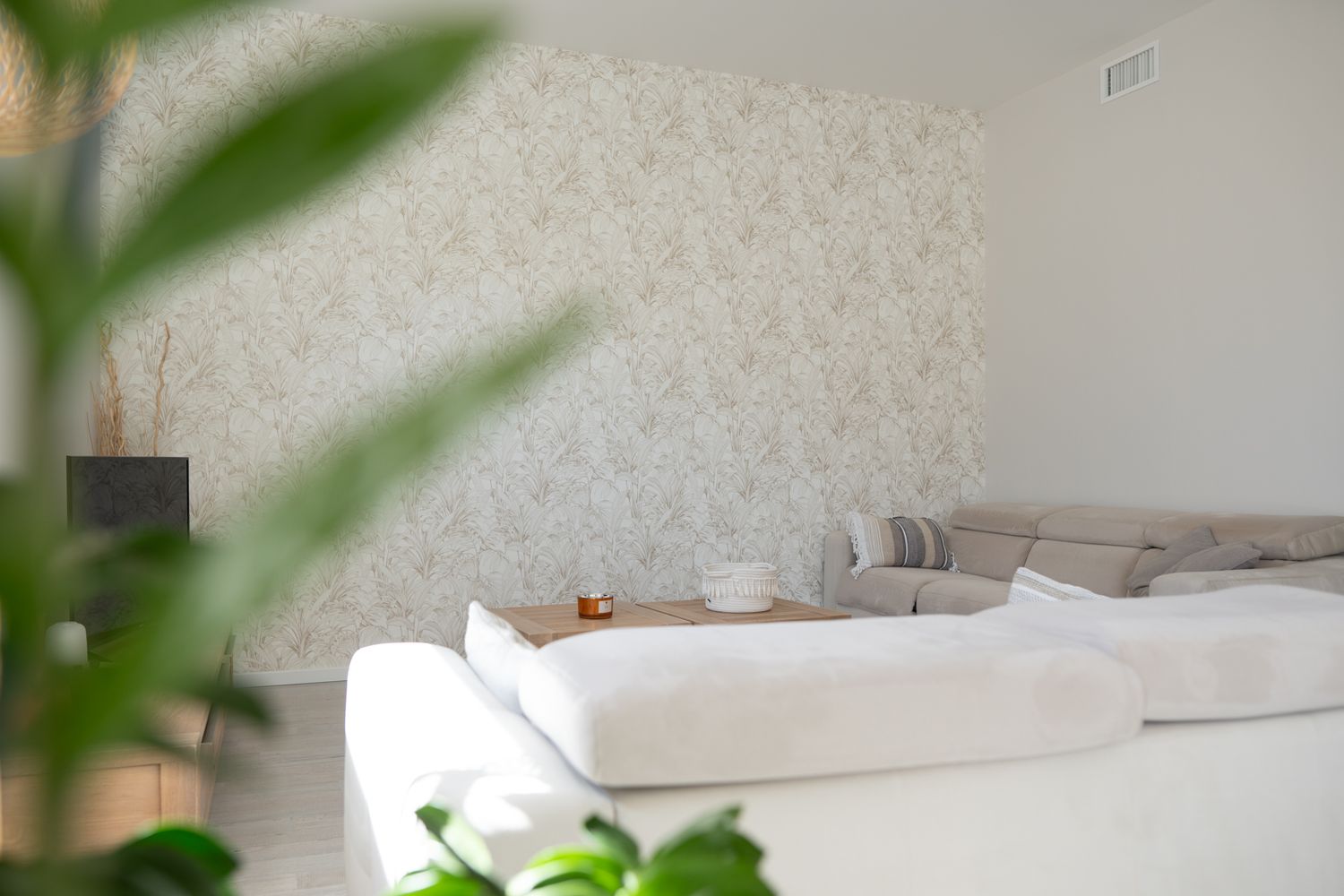 Modern bedroom interior with white walls, gray bedding, and green plant leaves framing the composition.
