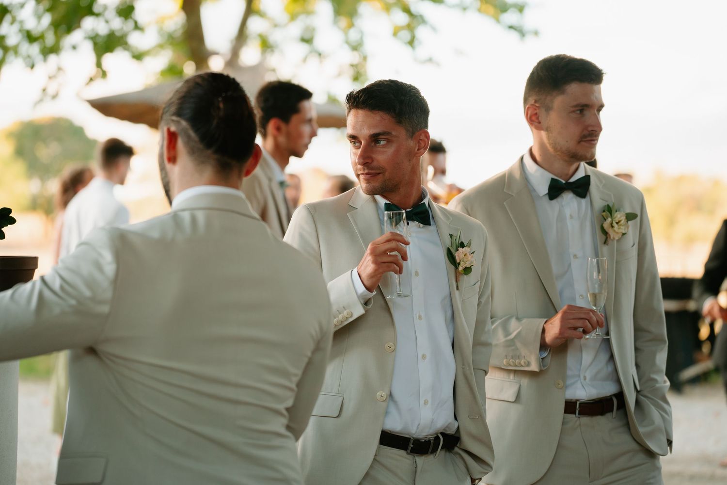 A group of people in white suits and formal attire mingle and socialize at an outdoor event.