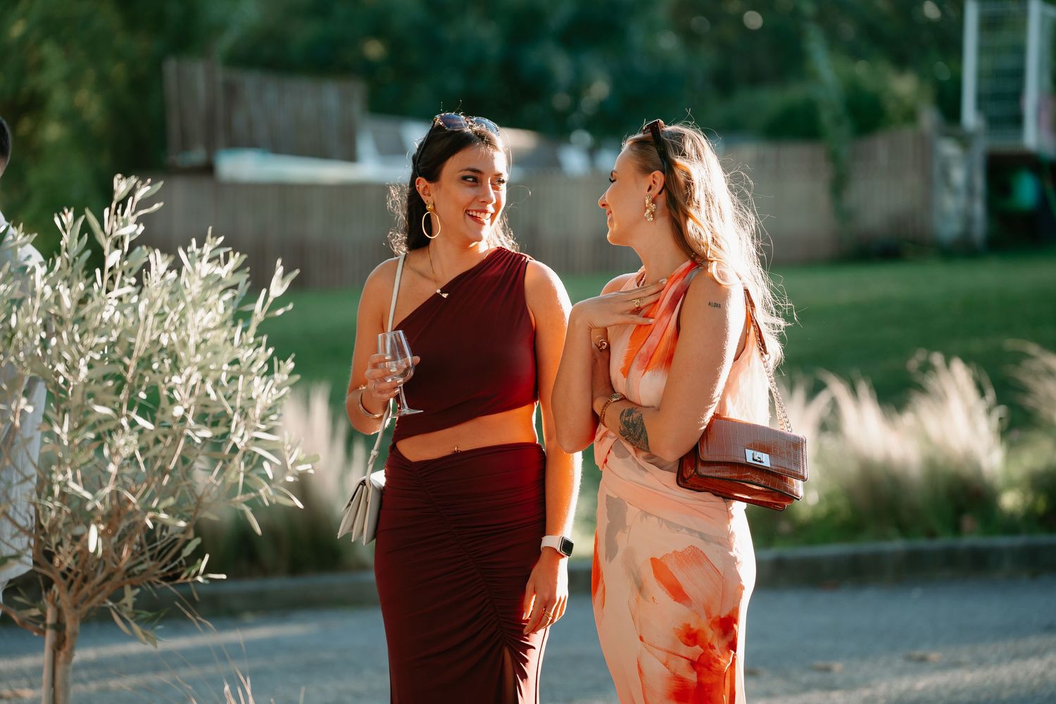 A couple in red and orange outfits dance together outdoors during golden hour with backlit grasses in the background.