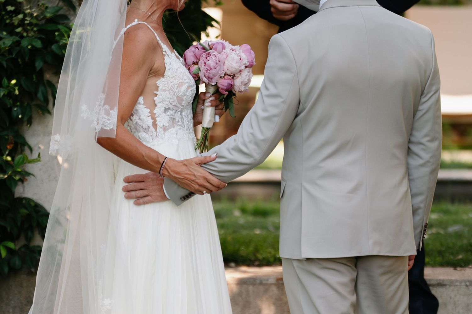 A close-up view of a bride and groom embracing, with the bride holding a pink bouquet and wearing a flowing white dress.