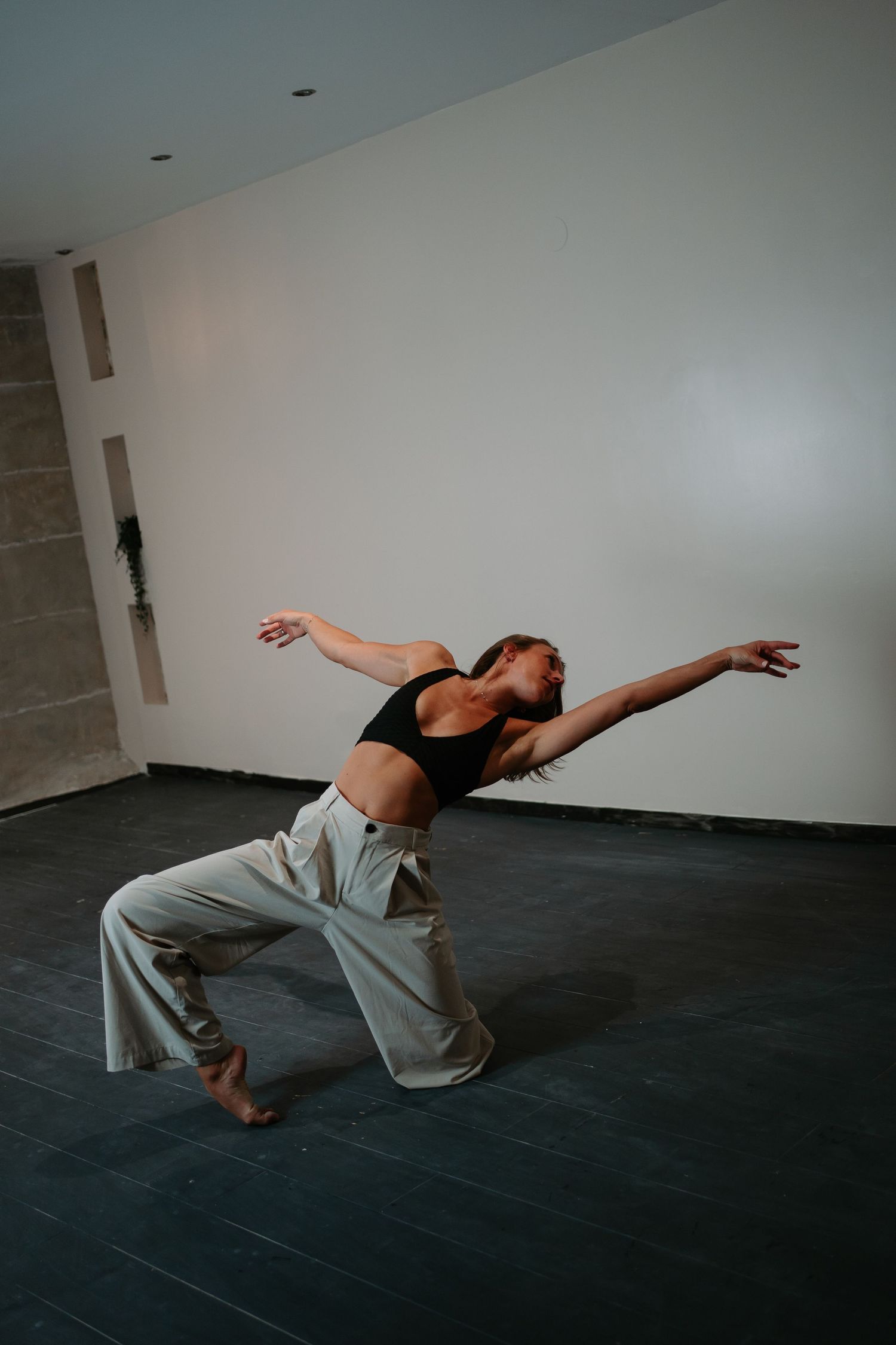Contemporary dancer performs expressive movements on dark floor against white wall in dramatic sequence.