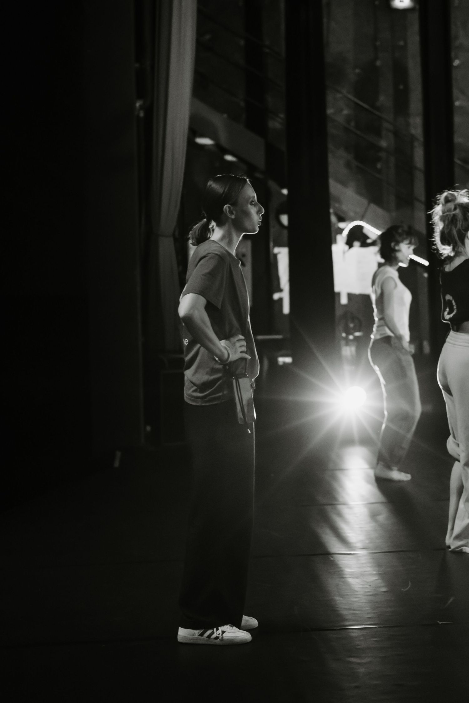 Dancers perform a dramatic sequence in a dimly lit studio space with striking backlighting creating silhouettes.
