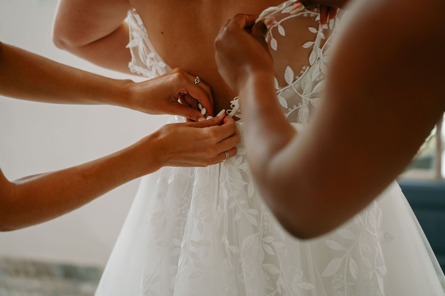 Close-up of hands helping to fasten buttons on the back of an elegant white wedding dress.
