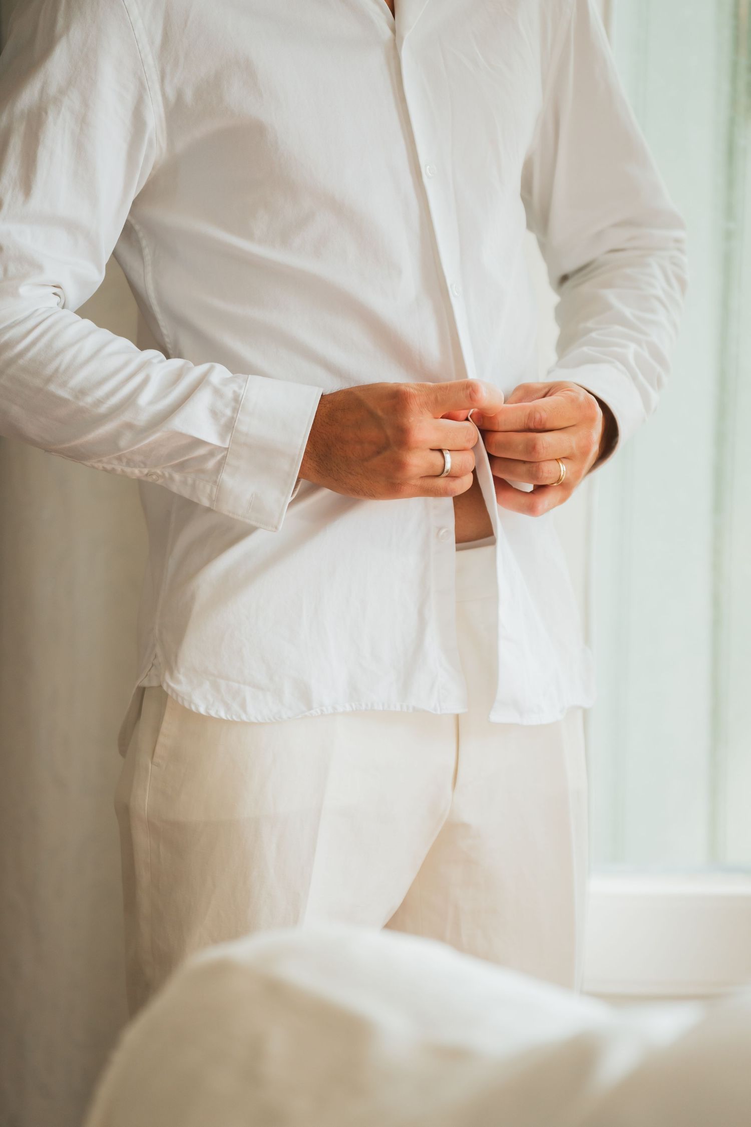 Close-up view of someone adjusting buttons on a crisp white dress shirt against a light background.