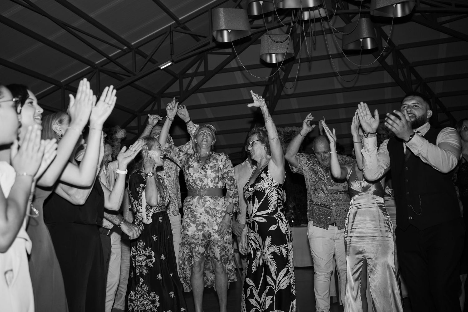 A black and white photo shows people dancing with their arms raised at a lively party celebration.