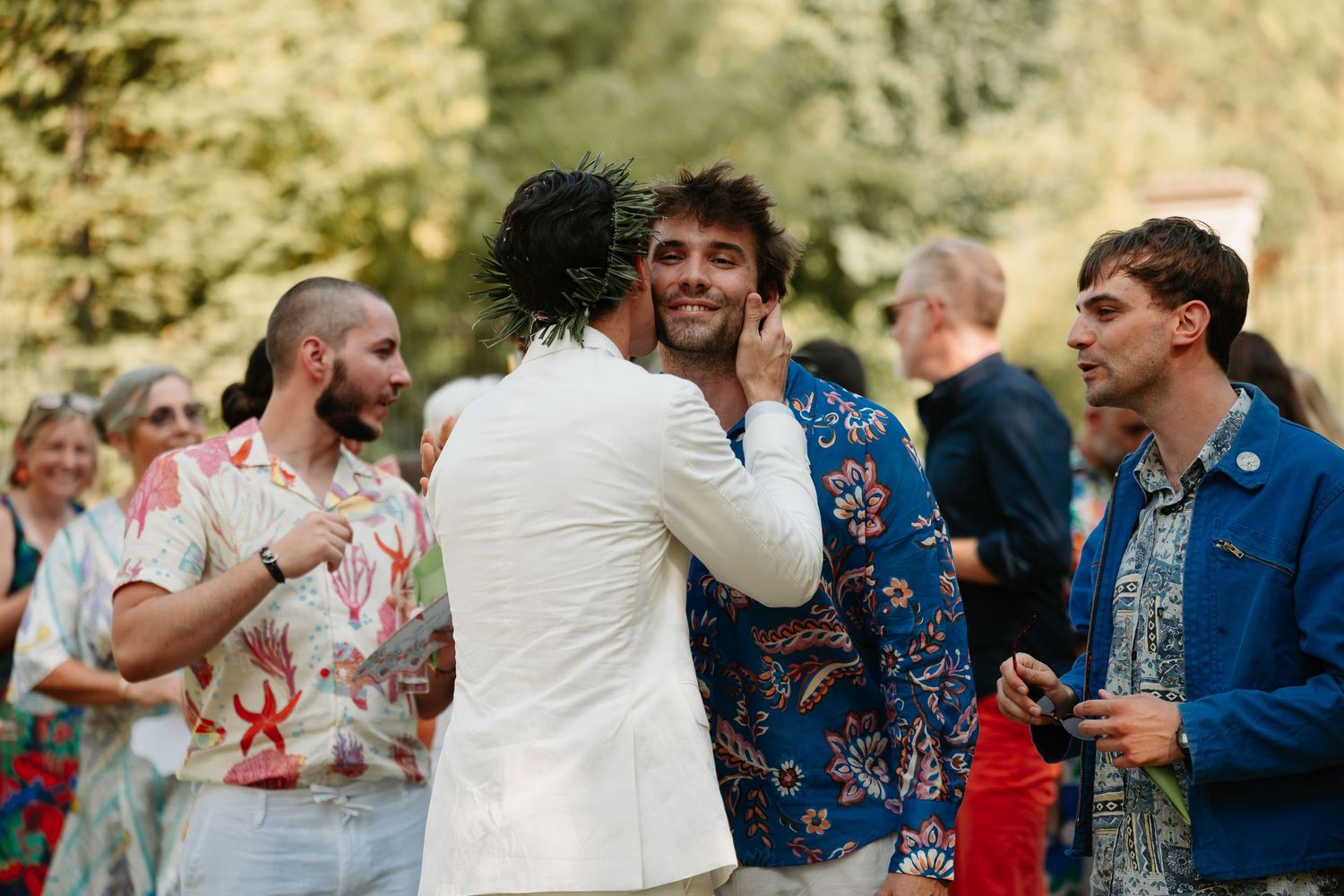 Wedding guests dance and celebrate together at an outdoor reception surrounded by trees and natural light.