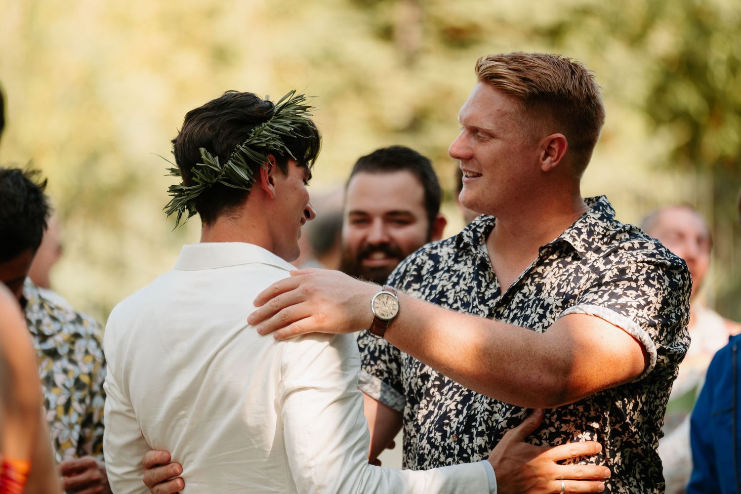 Wedding guests dance and embrace during outdoor celebration at sunset.