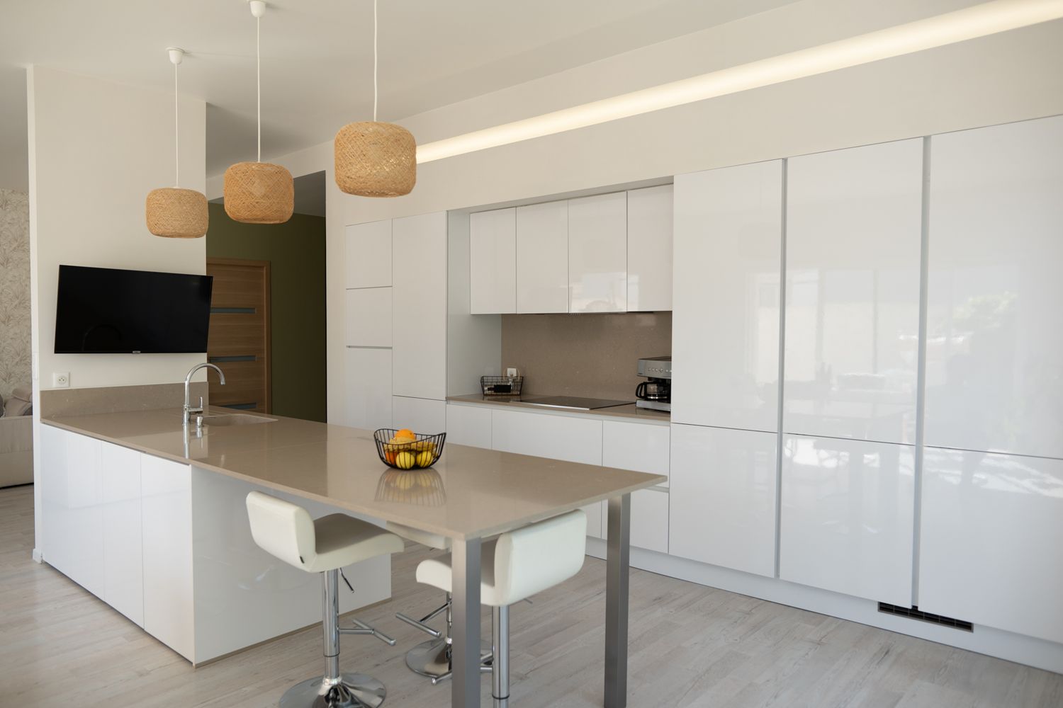 Modern white kitchen with sleek cabinetry, pendant lights, and a minimalist design features glossy surfaces and clean lines.
