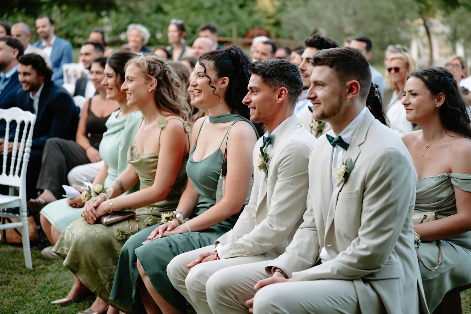 Wedding guests seated in rows of white chairs during an outdoor garden ceremony.