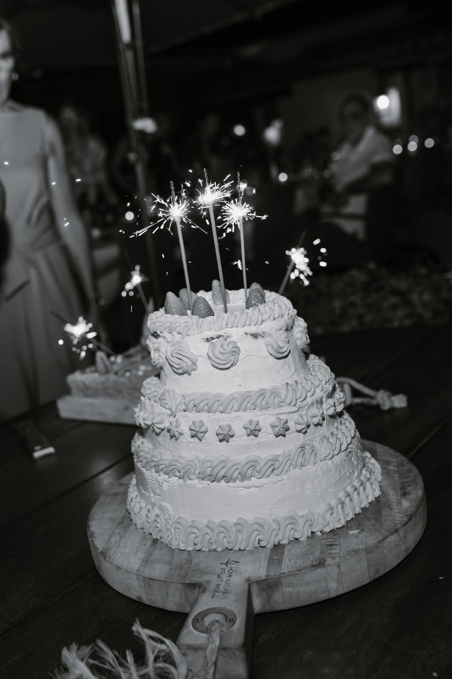 A black and white photo of a tiered wedding cake decorated with sparklers glowing on top at night.