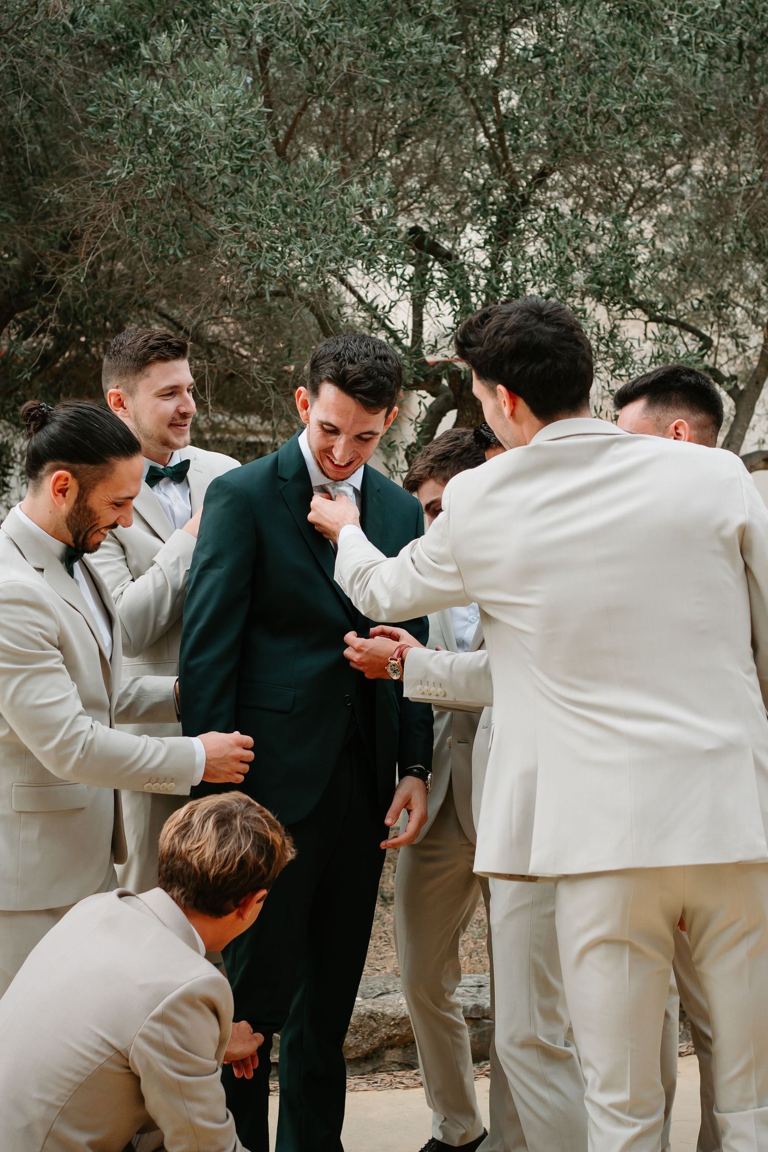 Groomsmen in white suits and one in black sharing playful moments in a sequence of candid wedding party photos.