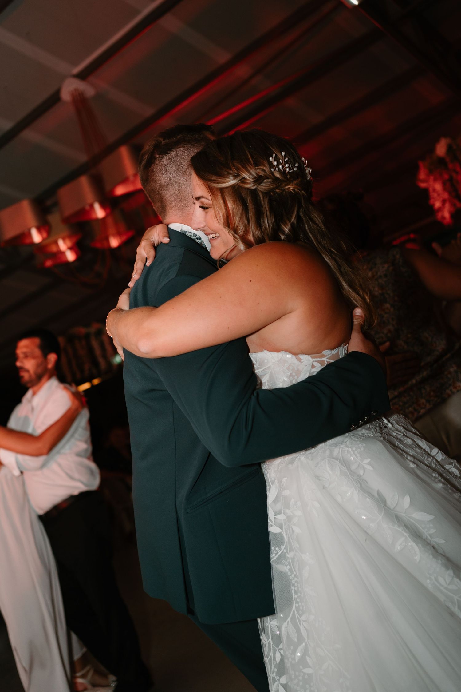 A couple shares an intimate dance moment at a wedding reception under moody red lighting.