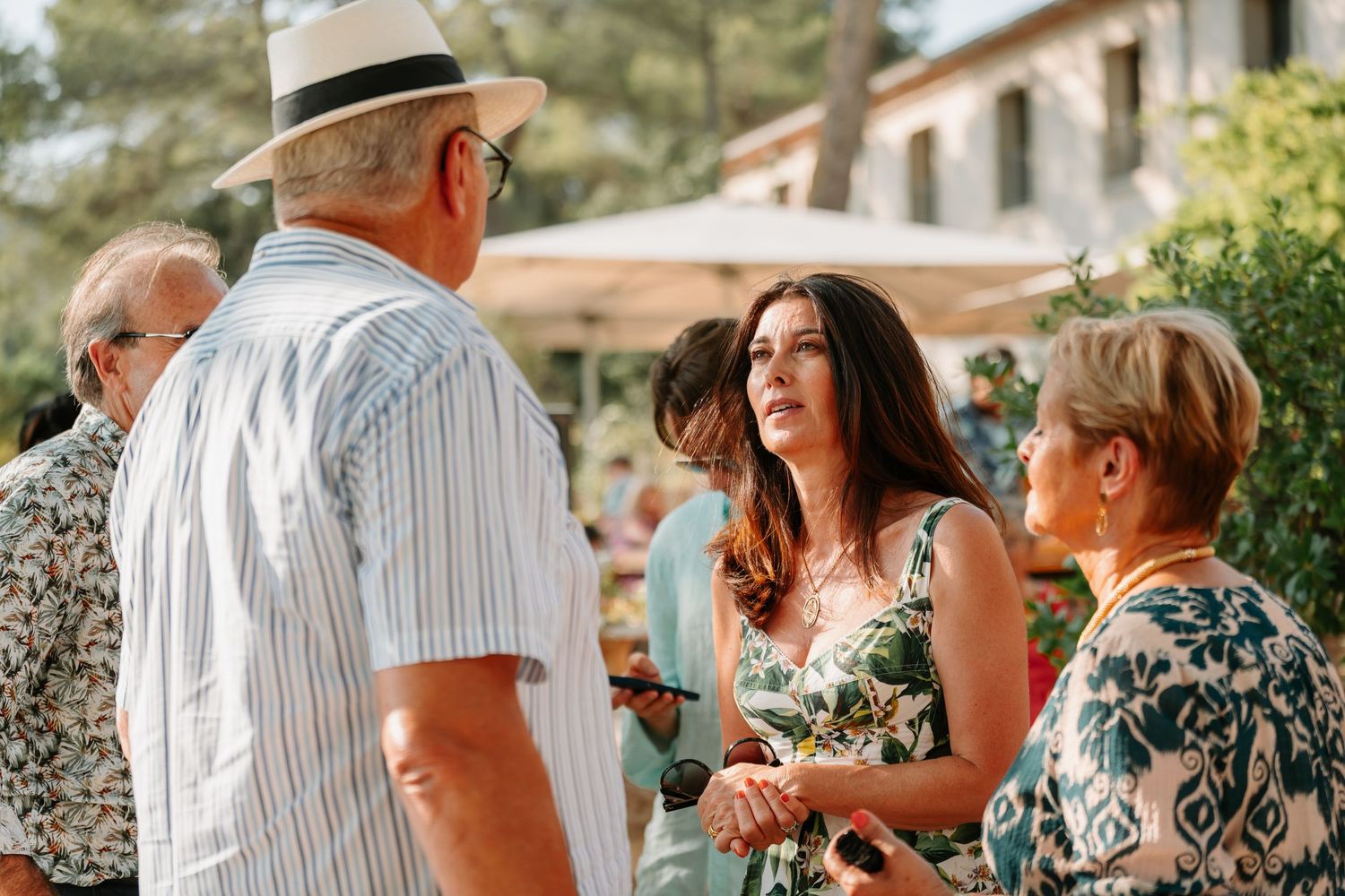 A group of people enjoying conversation and drinks at an outdoor summer gathering in a garden setting.