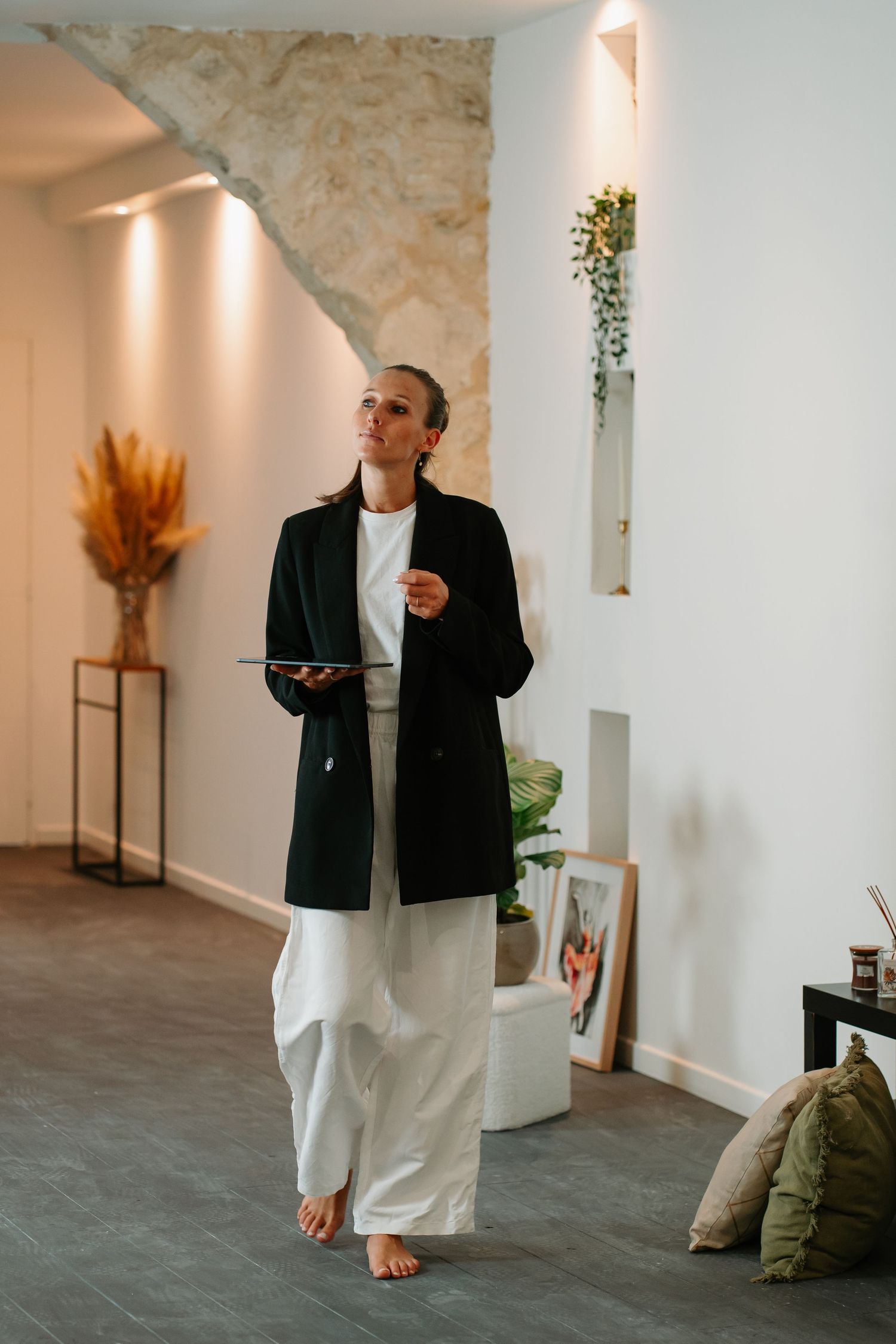 Person in black blazer and white pants walking through a modern gallery space with stone walls and spotlights.