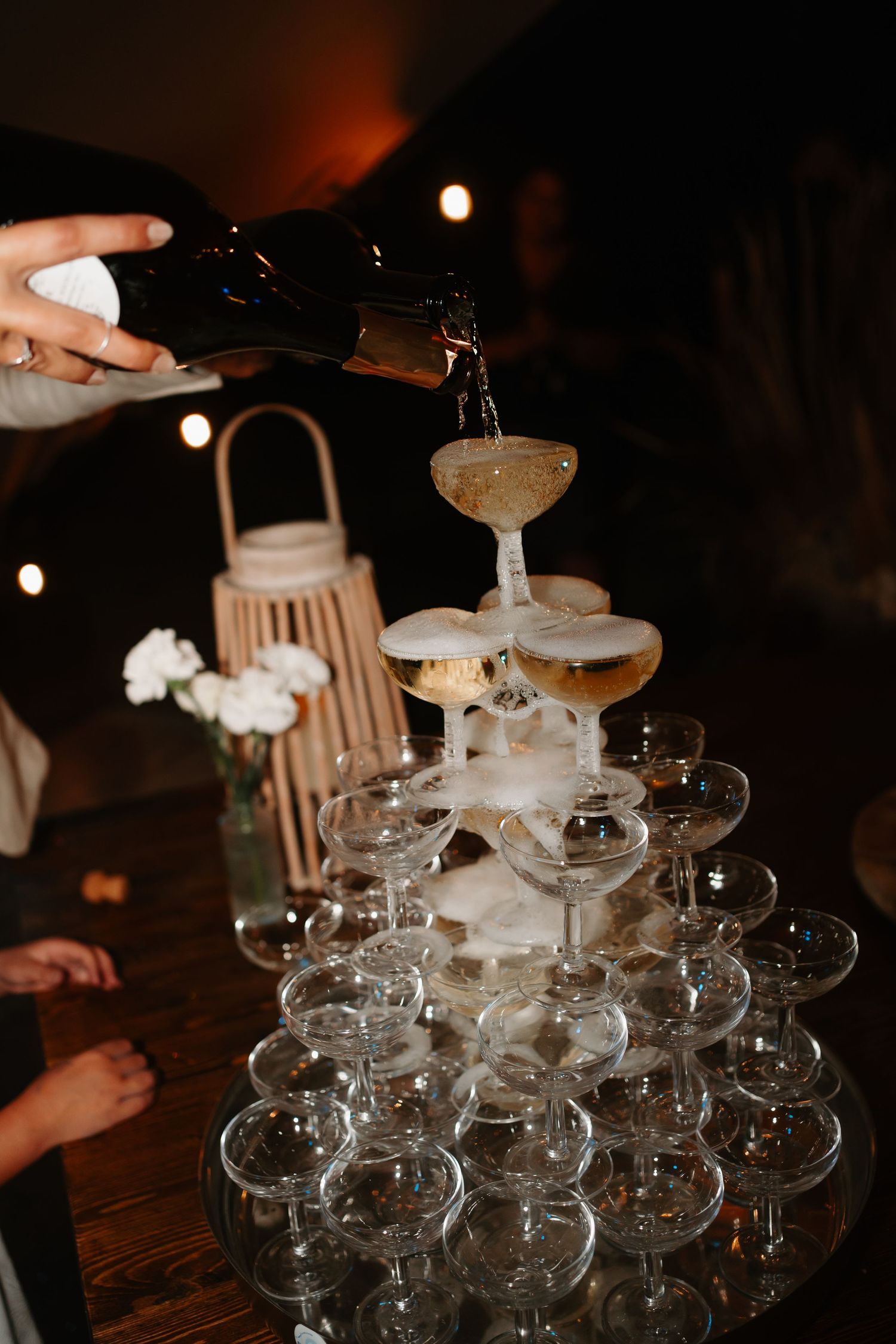 Champagne tower with coupe glasses being filled at dimly lit reception.