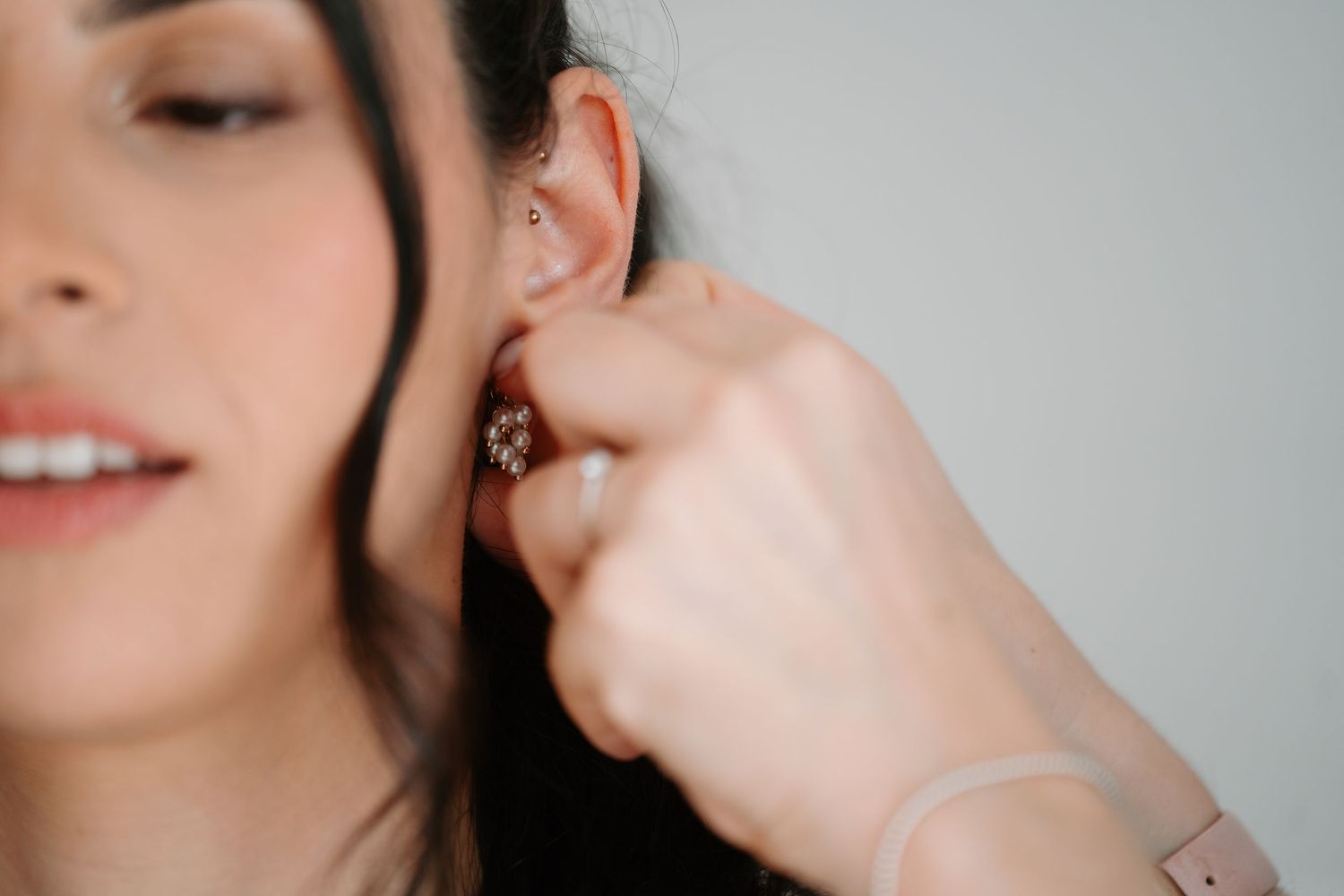 Close-up shot of someone putting on a delicate earring with dark hair visible in soft lighting.