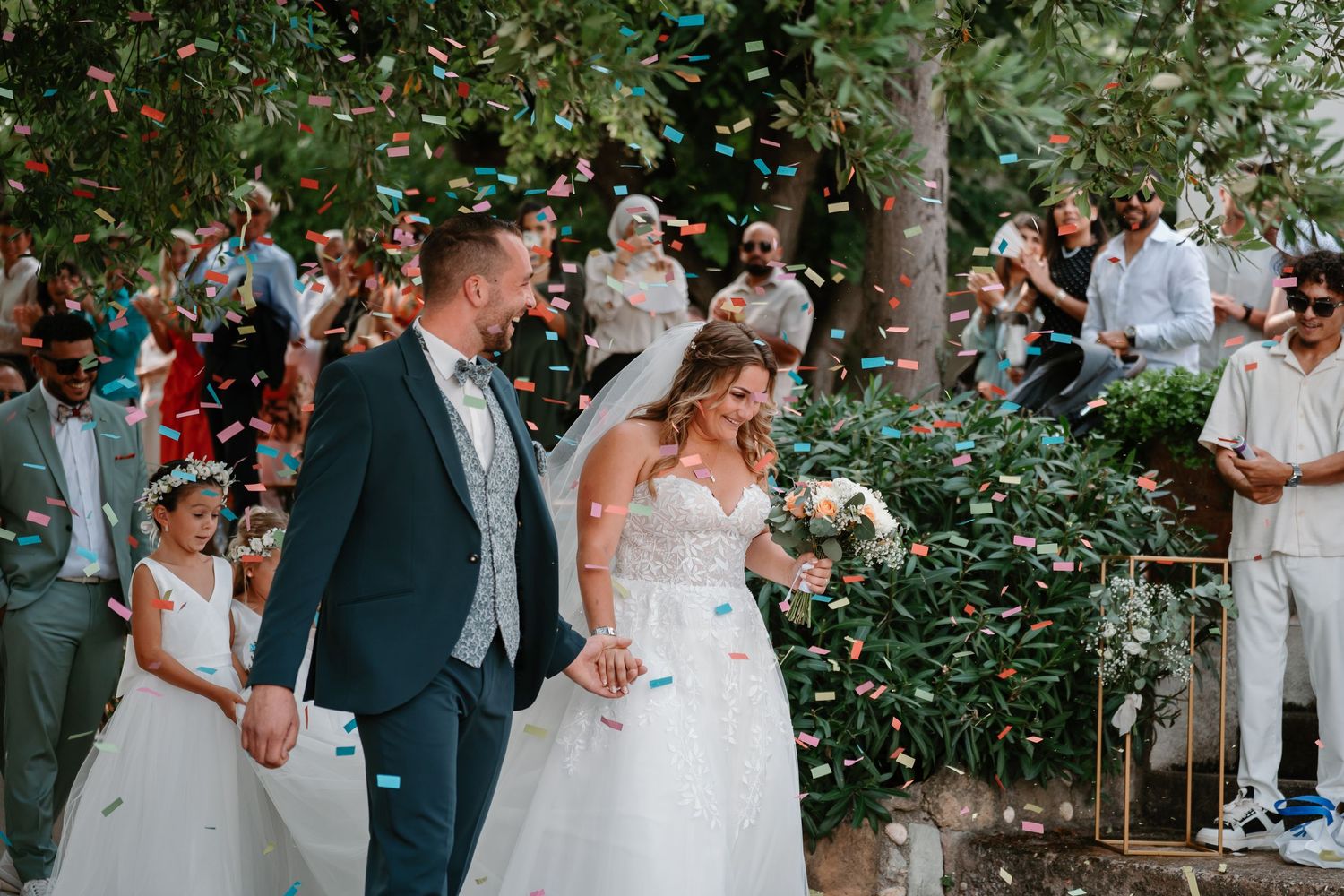 Wedding guests celebrate outdoors in a lush garden setting with fluttering confetti and joyful expressions.