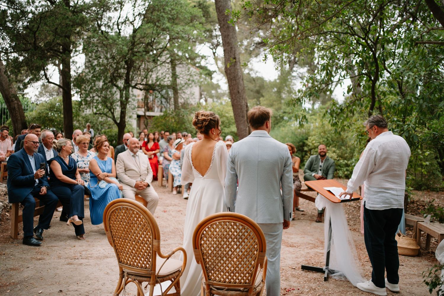 Outdoor wedding ceremony in a forest setting with guests seated as bride and groom stand before officiant.