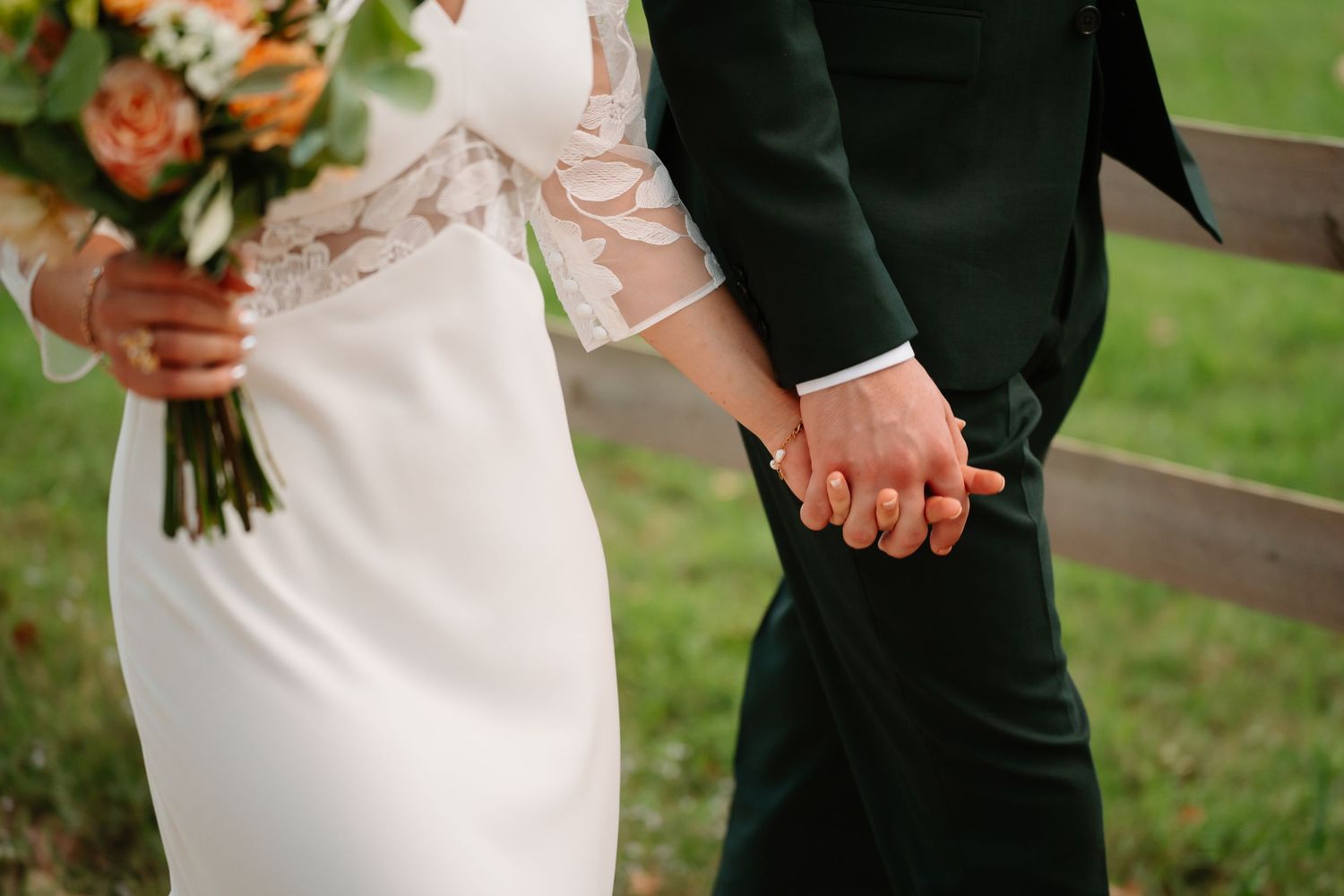 Bride and groom hold hands during outdoor wedding ceremony with lush greenery in background.