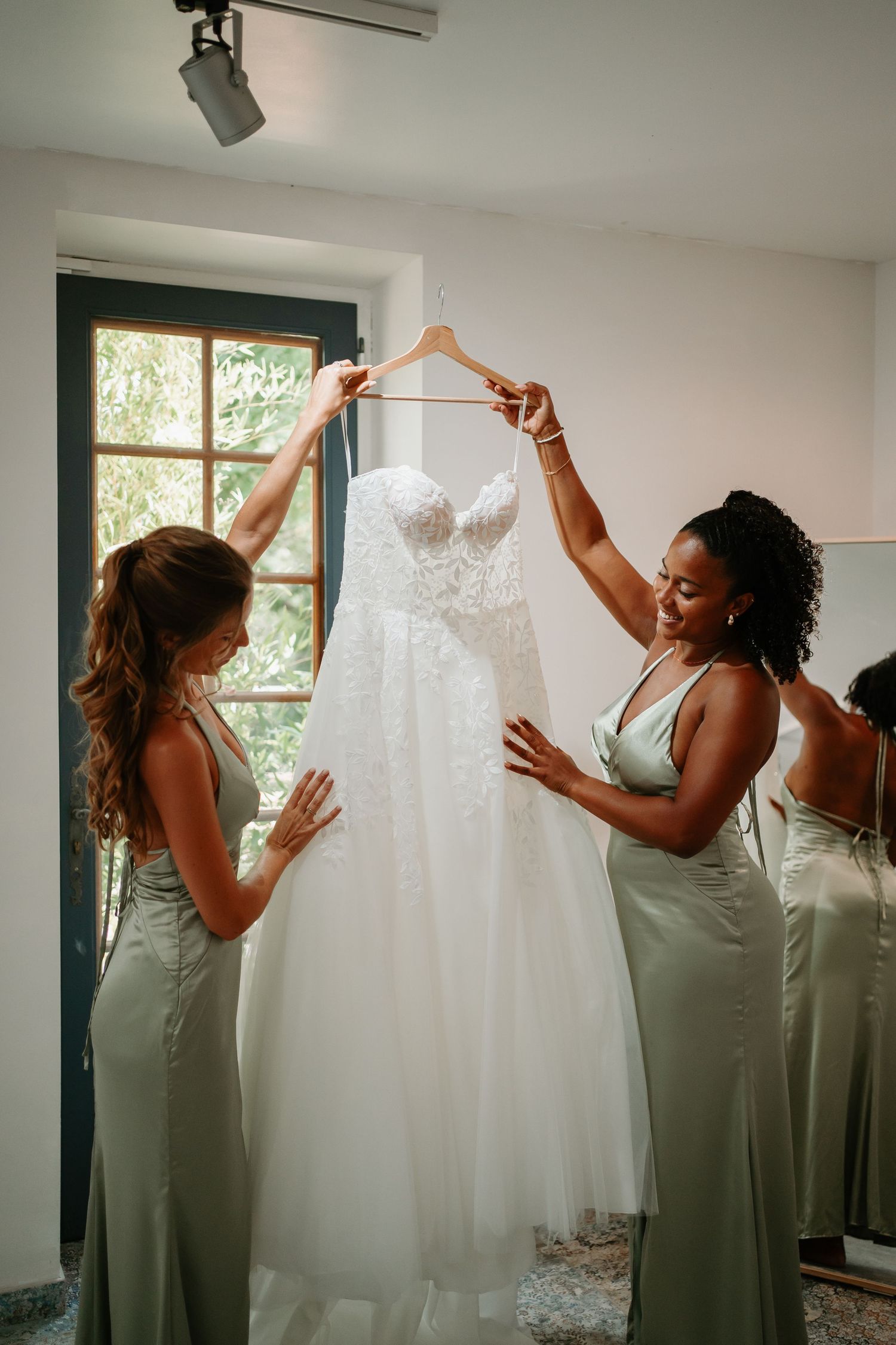 Wedding party attendants in sage green dresses help lift and display a white wedding gown in a sequence of photos.