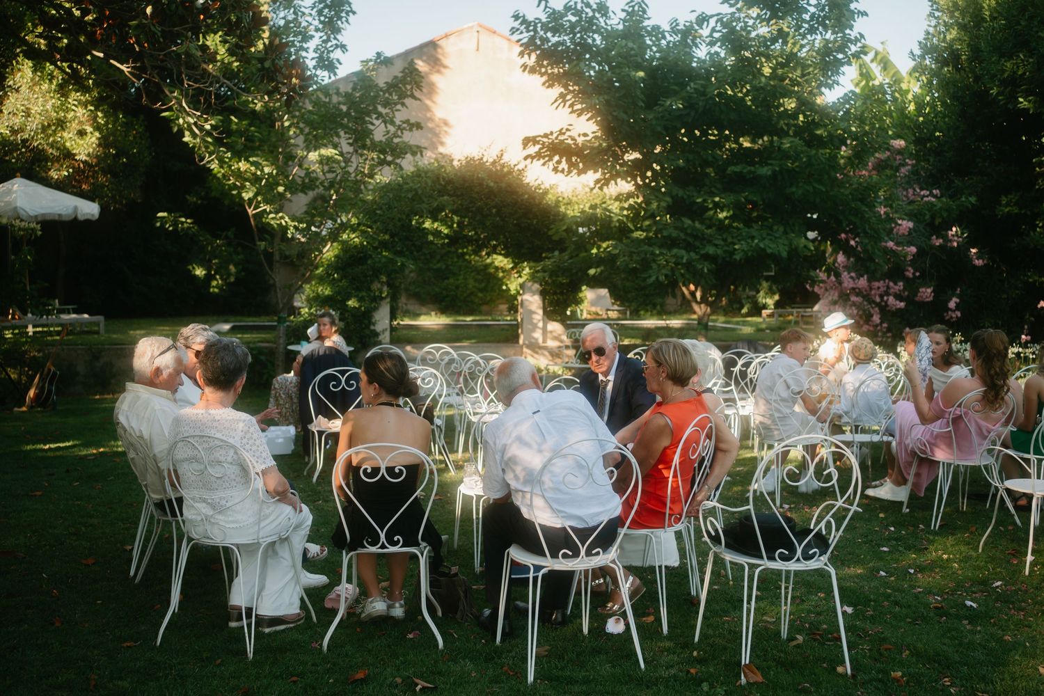 Guests seated at white outdoor tables during a sunset garden party celebration.