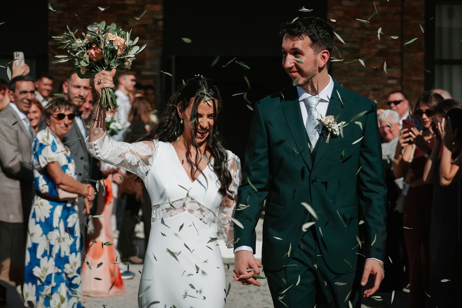 Wedding guests shower happy newlyweds with white confetti as they exit the church ceremony together.