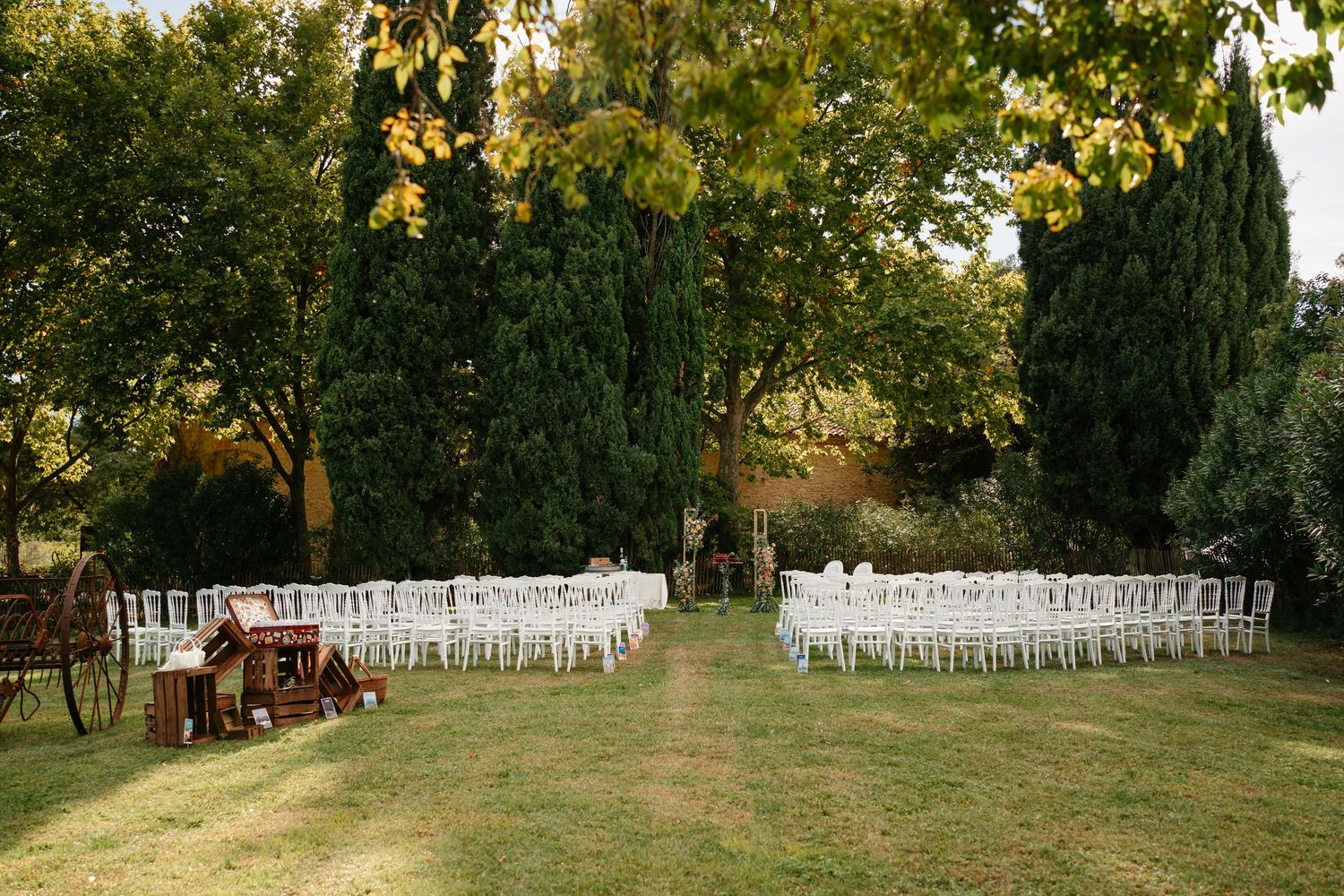 White wedding chairs arranged in rows on a grassy lawn for an outdoor ceremony with trees in the background.