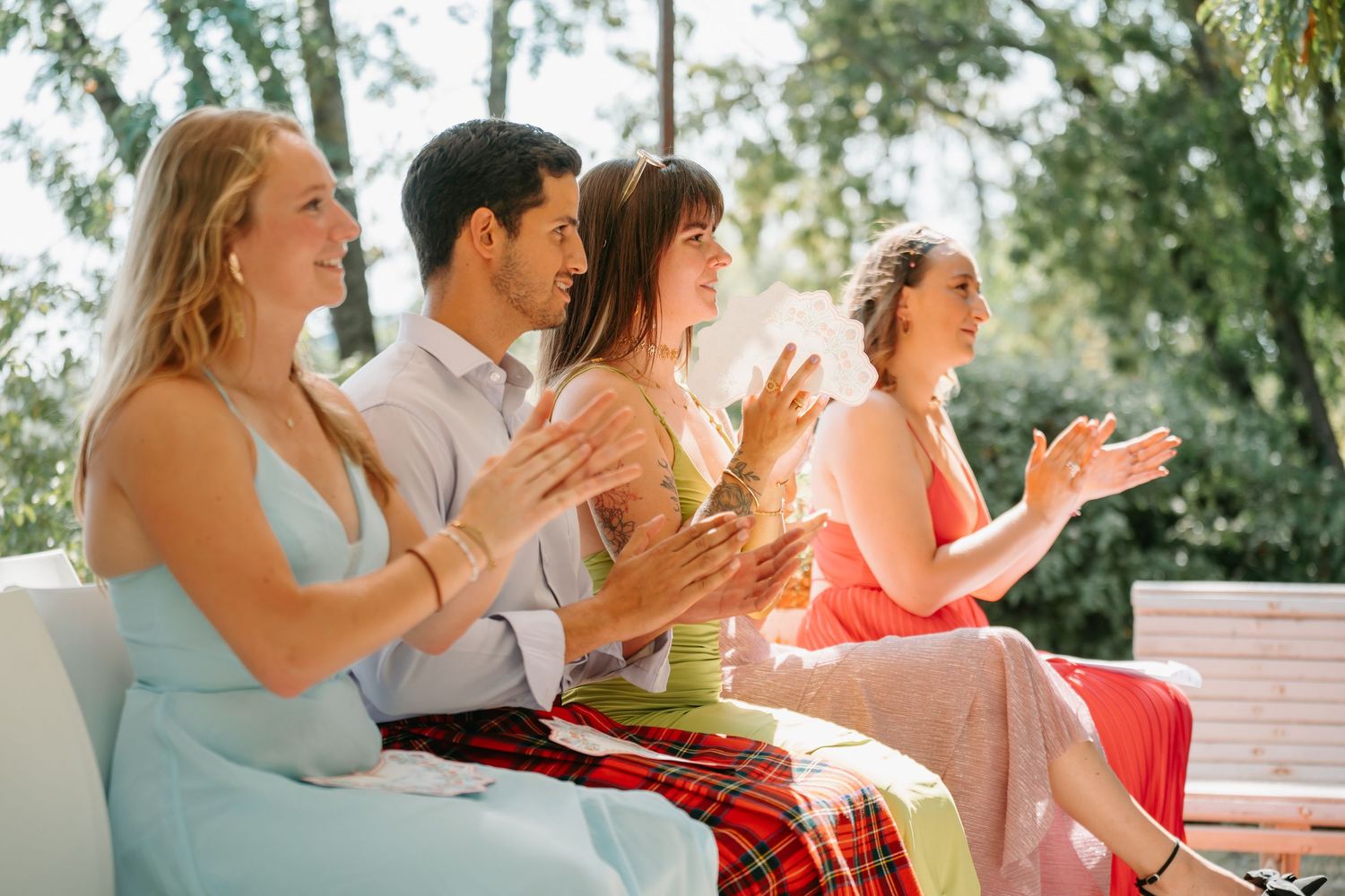 A group of people sitting outdoors clapping and celebrating together during a sunny afternoon gathering.