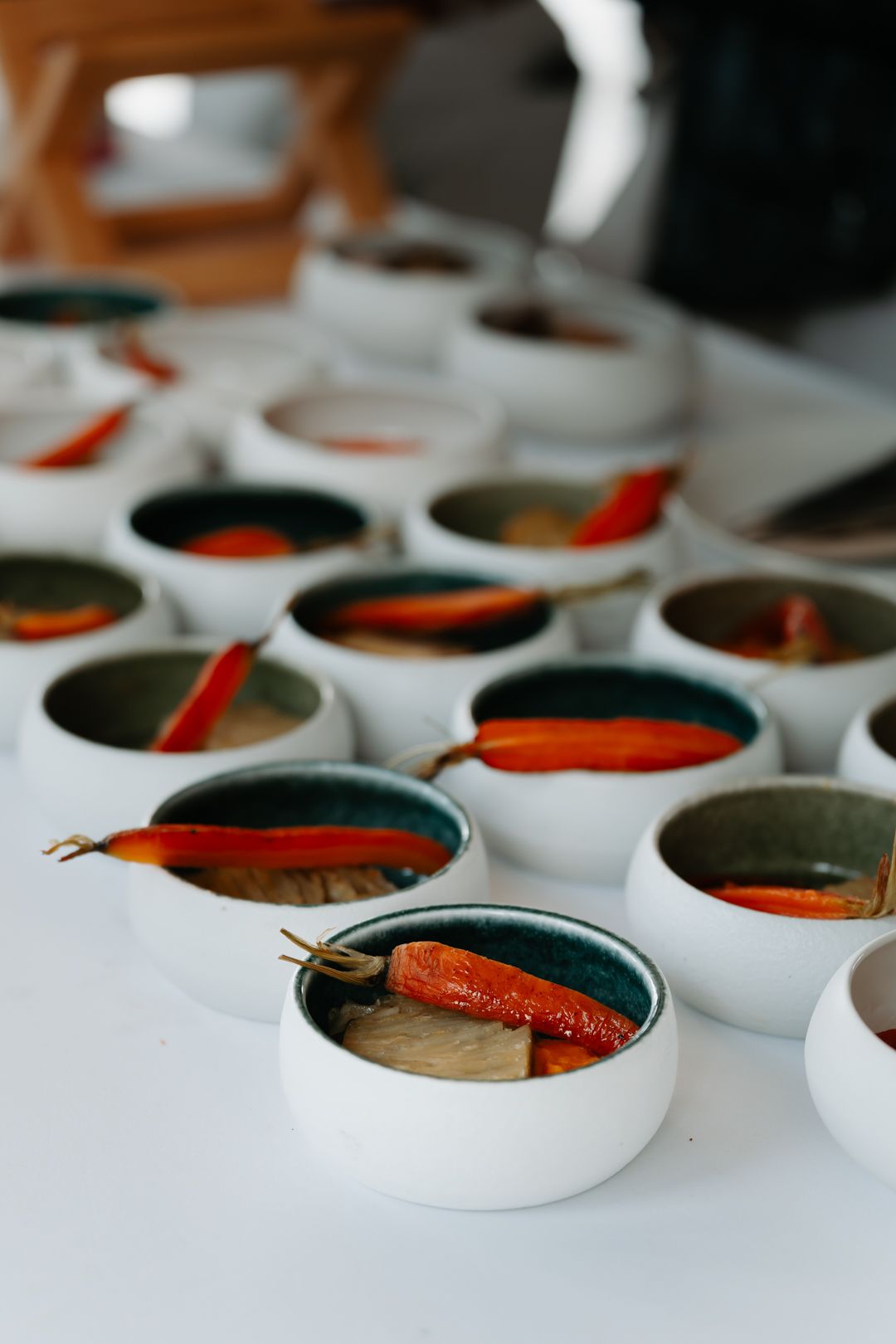 Row of small white bowls containing artfully plated dishes with orange and dark elements.