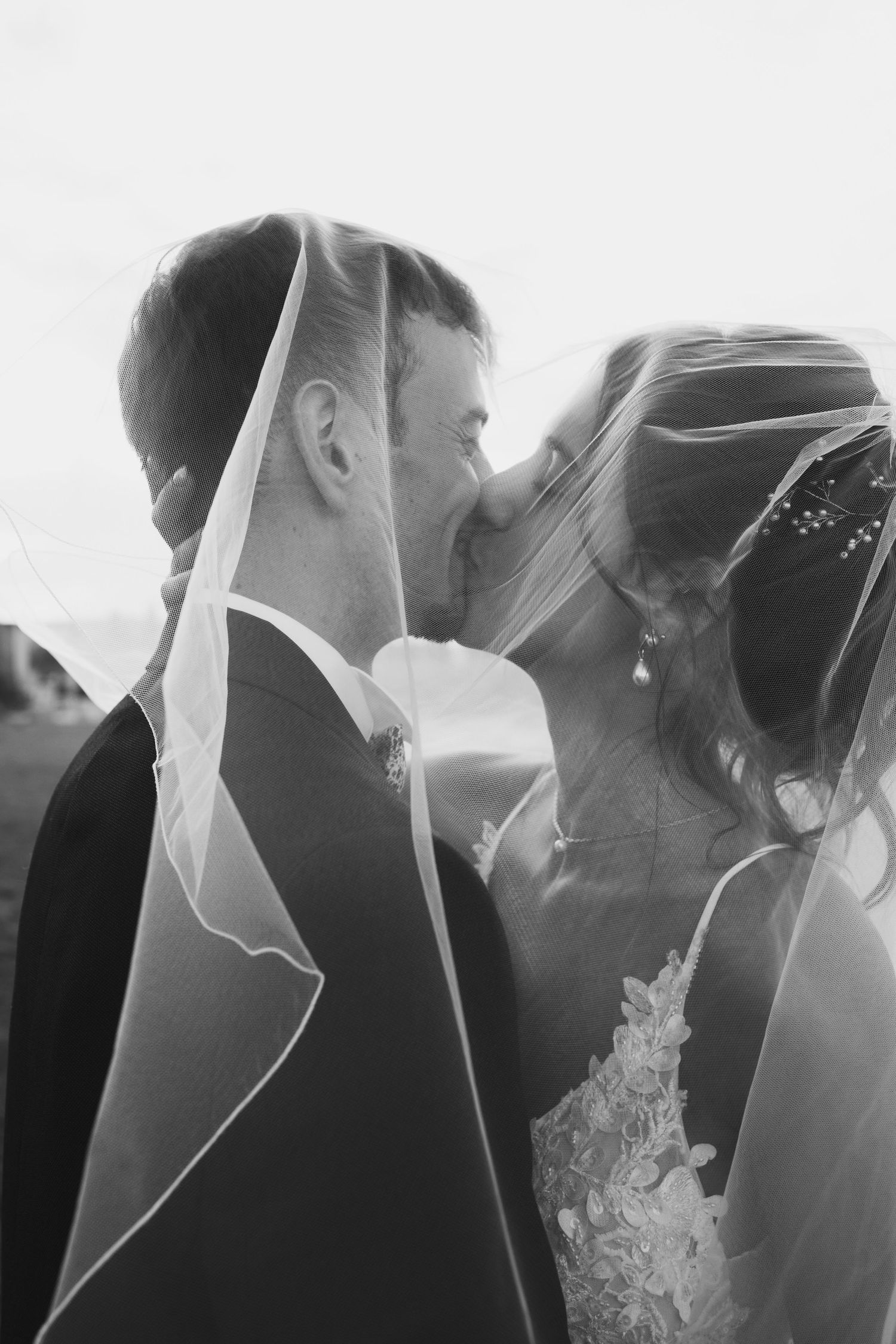 Romantic black and white portrait of a wedding couple sharing an intimate veiled moment.