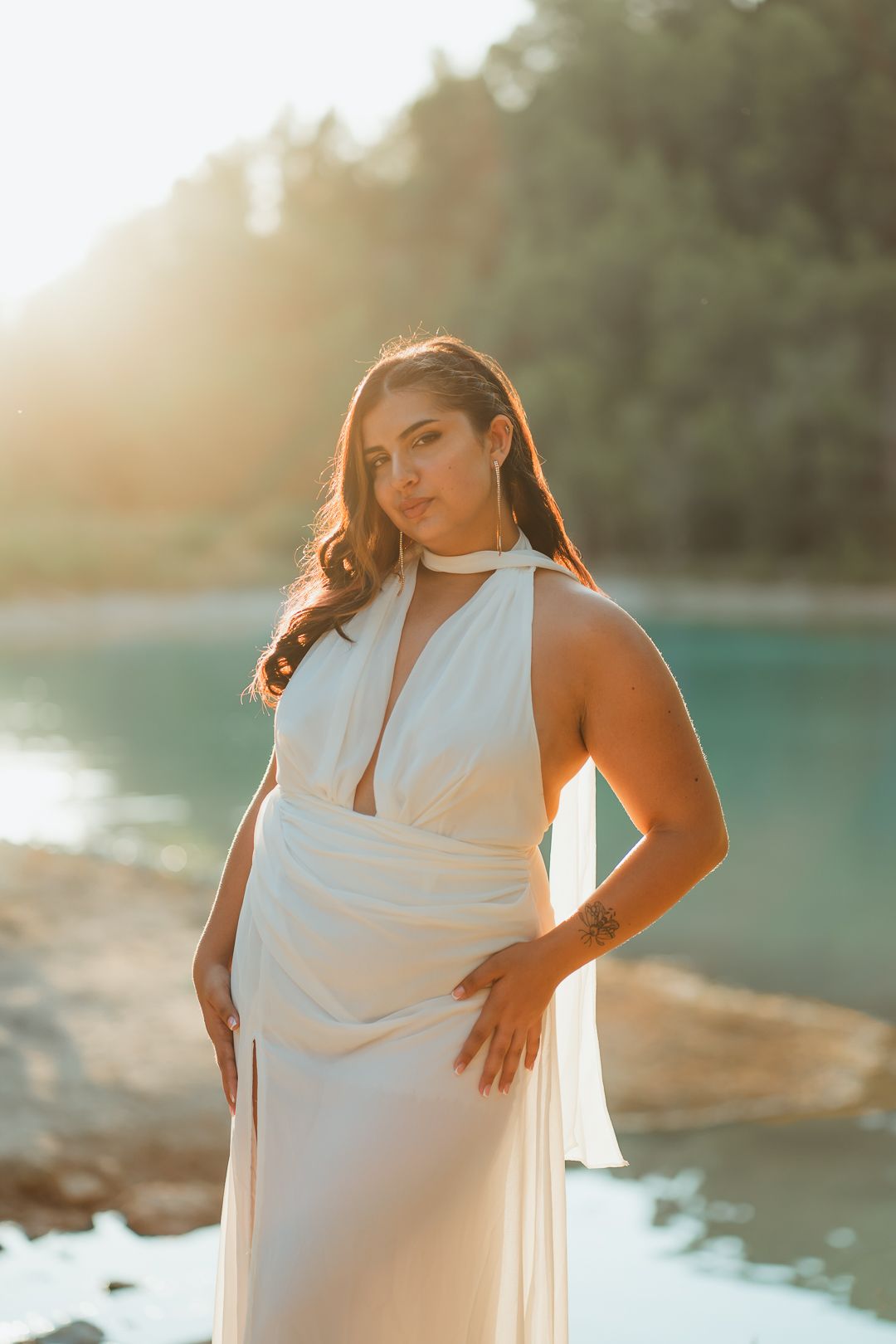 Beautiful beach portrait at sunset featuring a flowing white halter dress and golden sunlight reflecting off the water.