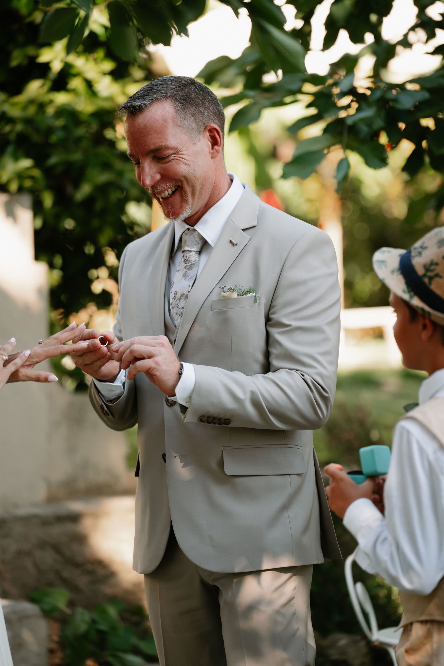 A person in a light gray suit jacket reacts emotionally during what appears to be a special outdoor occasion.
