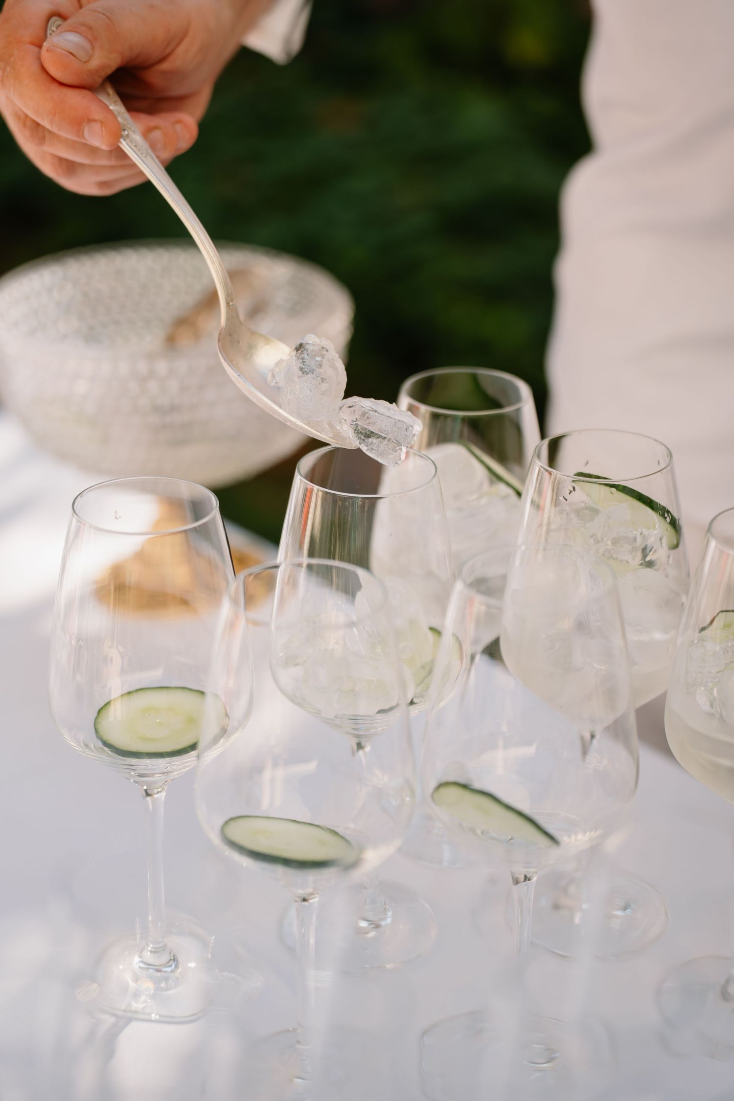 Pouring clear cocktails into elegant martini glasses with cucumber garnish at an upscale event.