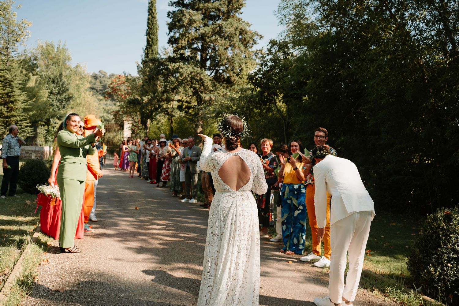 Wedding guests line up on a garden path to greet newlyweds in a backyard ceremony setting.
