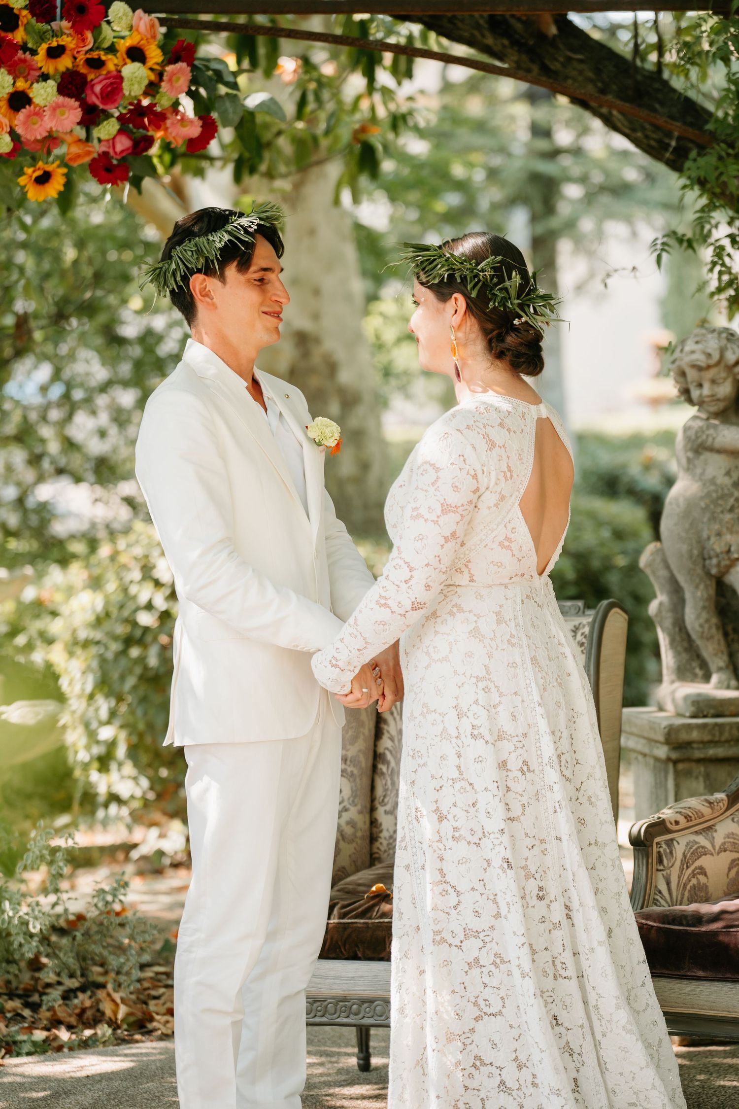 A couple in elegant white attire shares romantic moments in a garden setting during their wedding photoshoot.