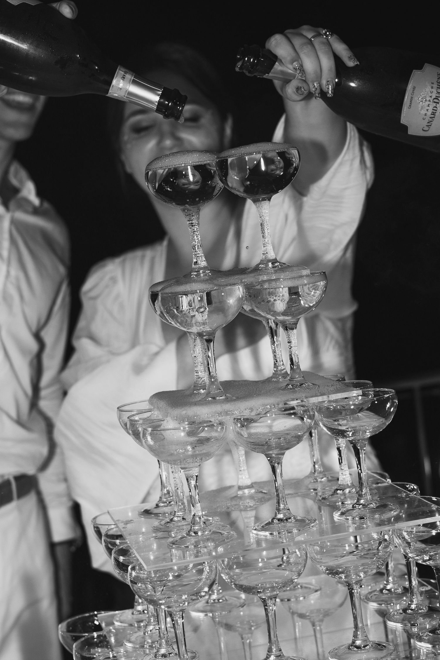 Hands carefully stack delicate champagne glasses into an elegant tower formation at a formal event.