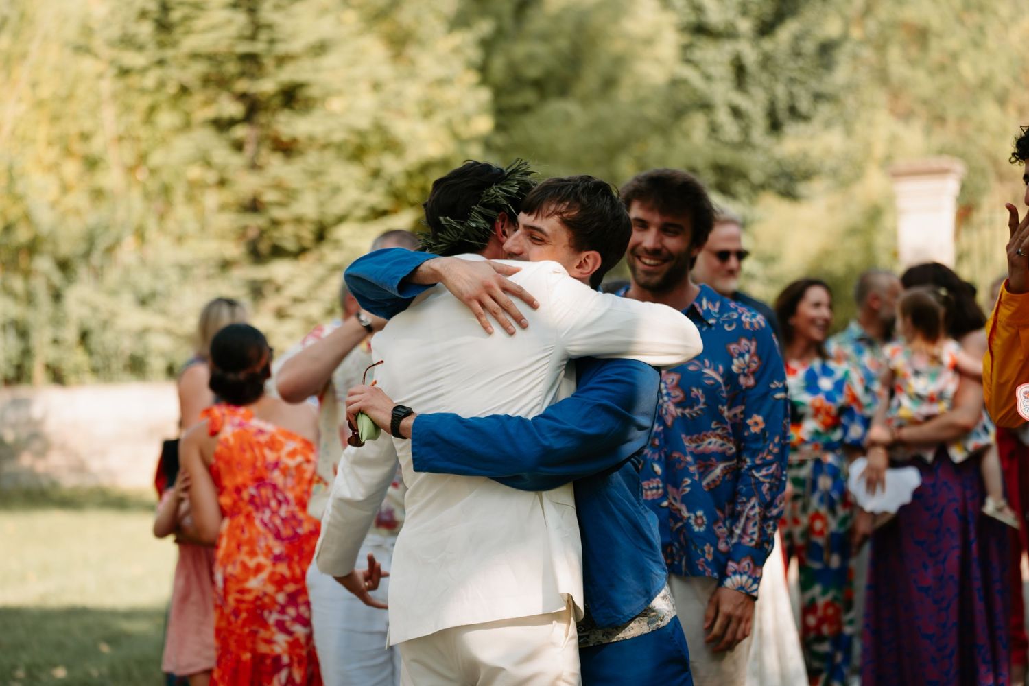 Wedding guests embrace and celebrate during an outdoor reception in a natural setting.