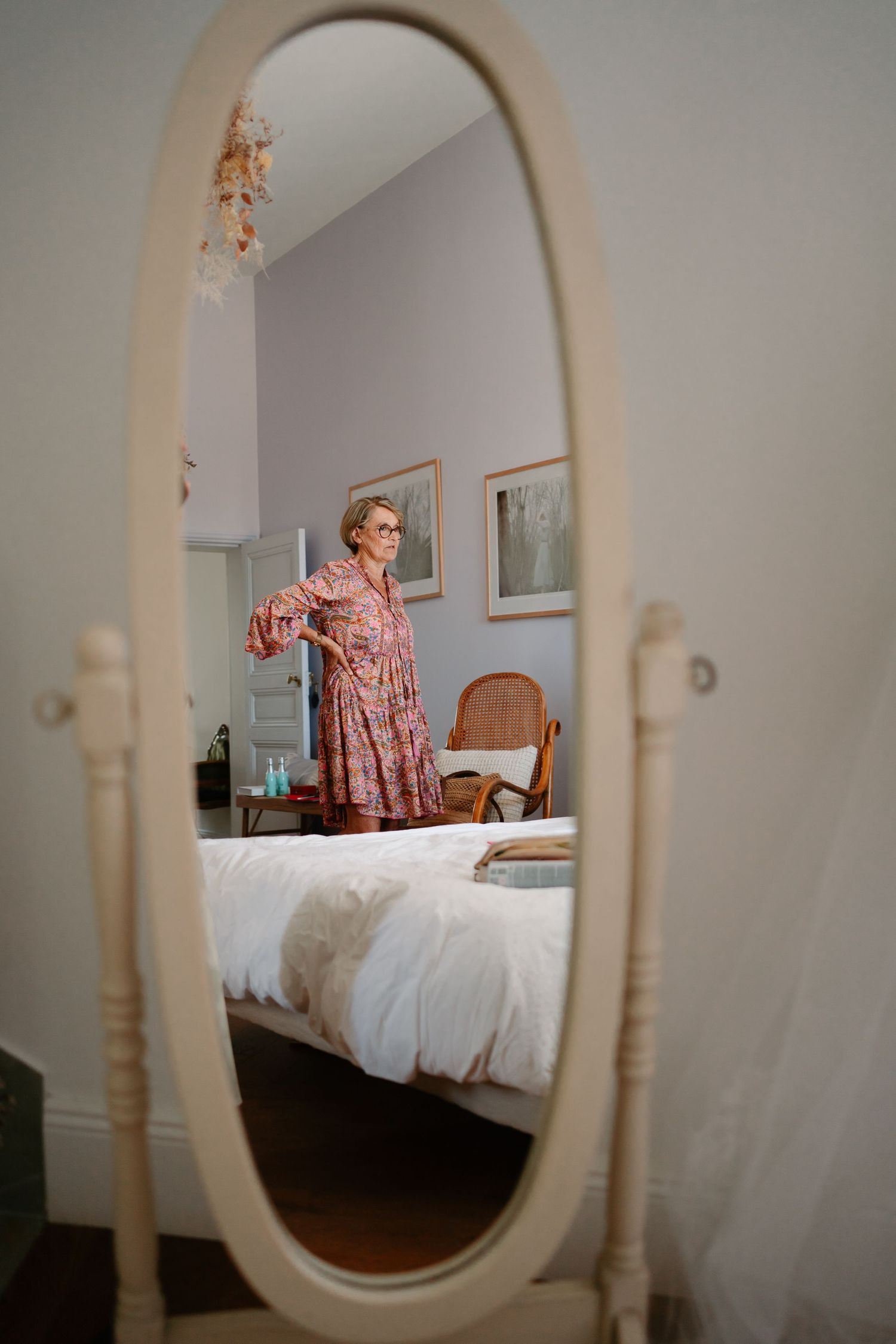 A series of mirror reflections shows a person in pink sitting on a bed in a bedroom with white walls and wooden furniture.