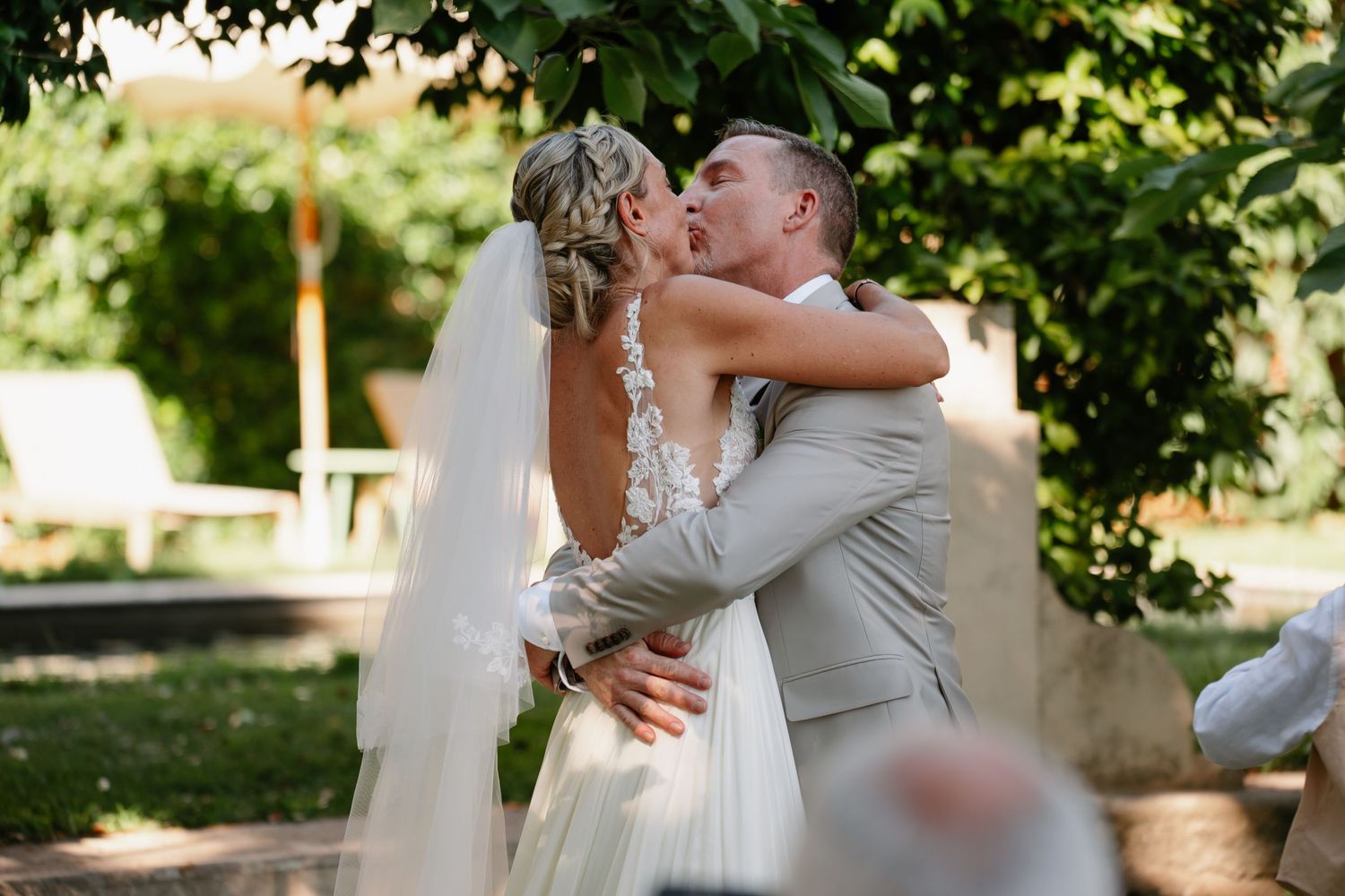 A couple shares a romantic kiss in an outdoor garden setting during their wedding celebration.