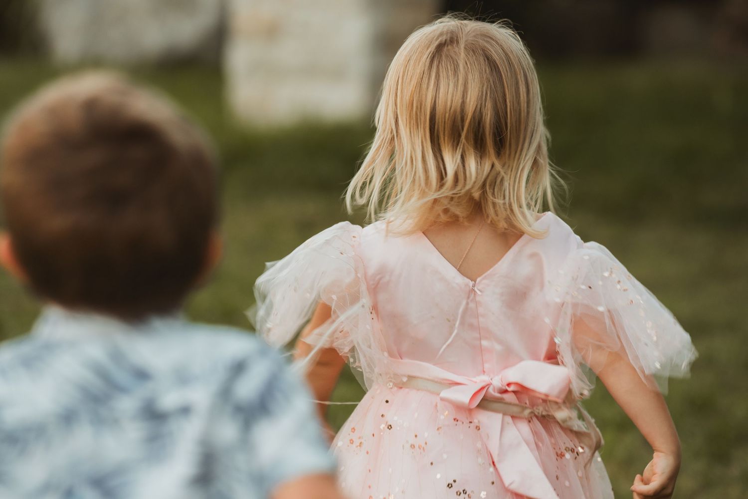 Wedding party members in pastel dresses walking through a garden setting.