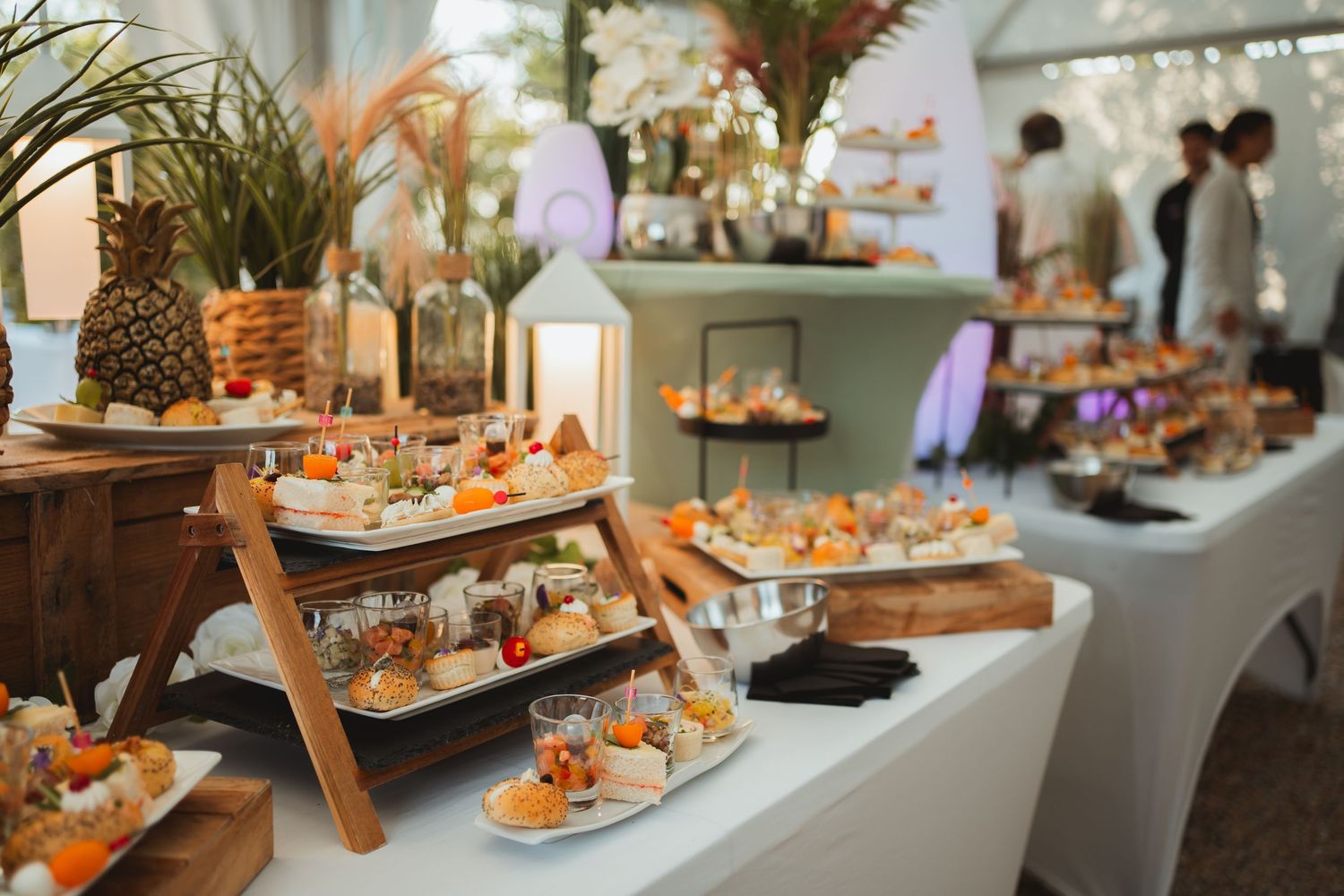Wedding catering display with wooden serving platters and decorative greenery arrangements.